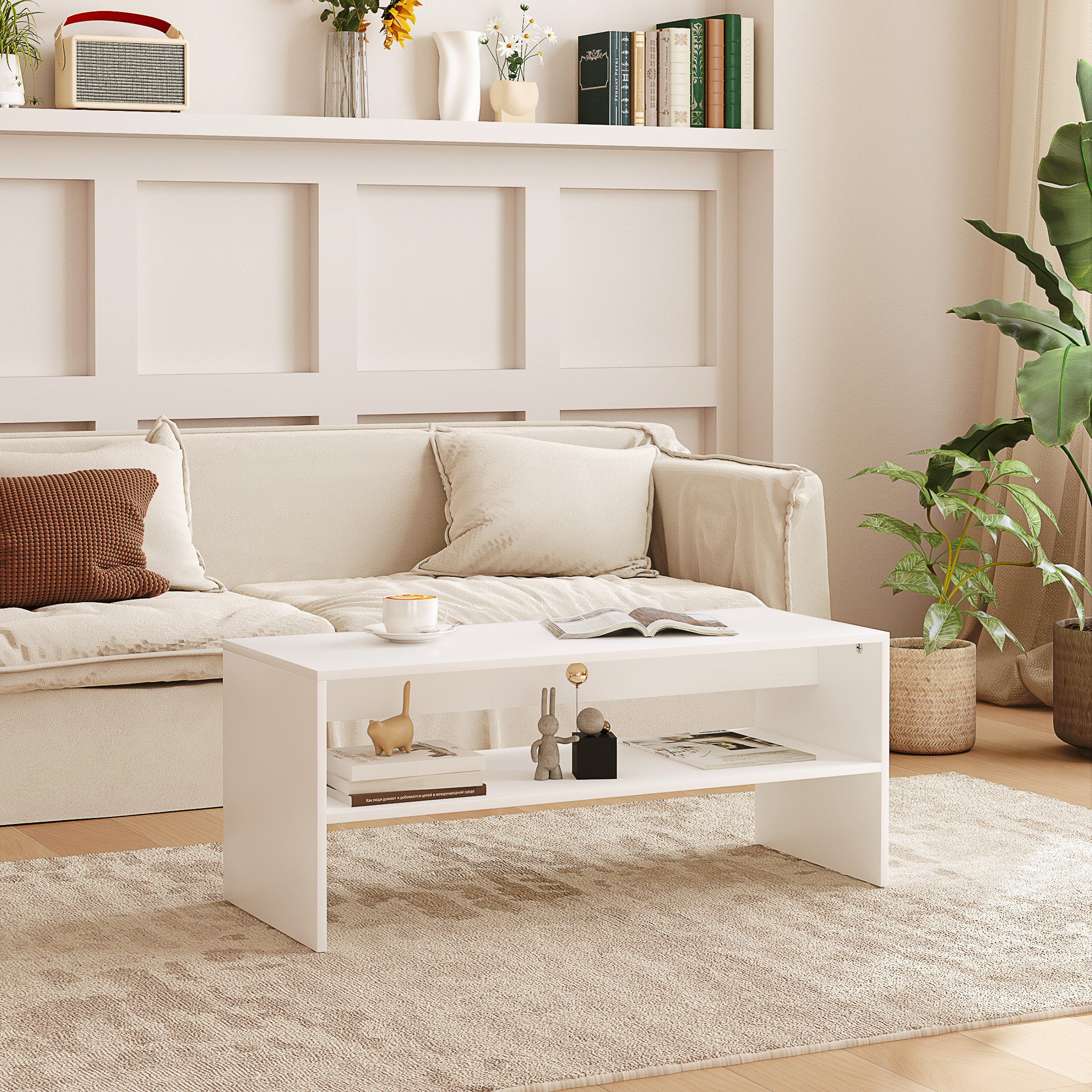 Un tavolino bianco davanti a un divano. Ha un ripiano inferiore con libri e decorazioni. Sfondo chiaro.