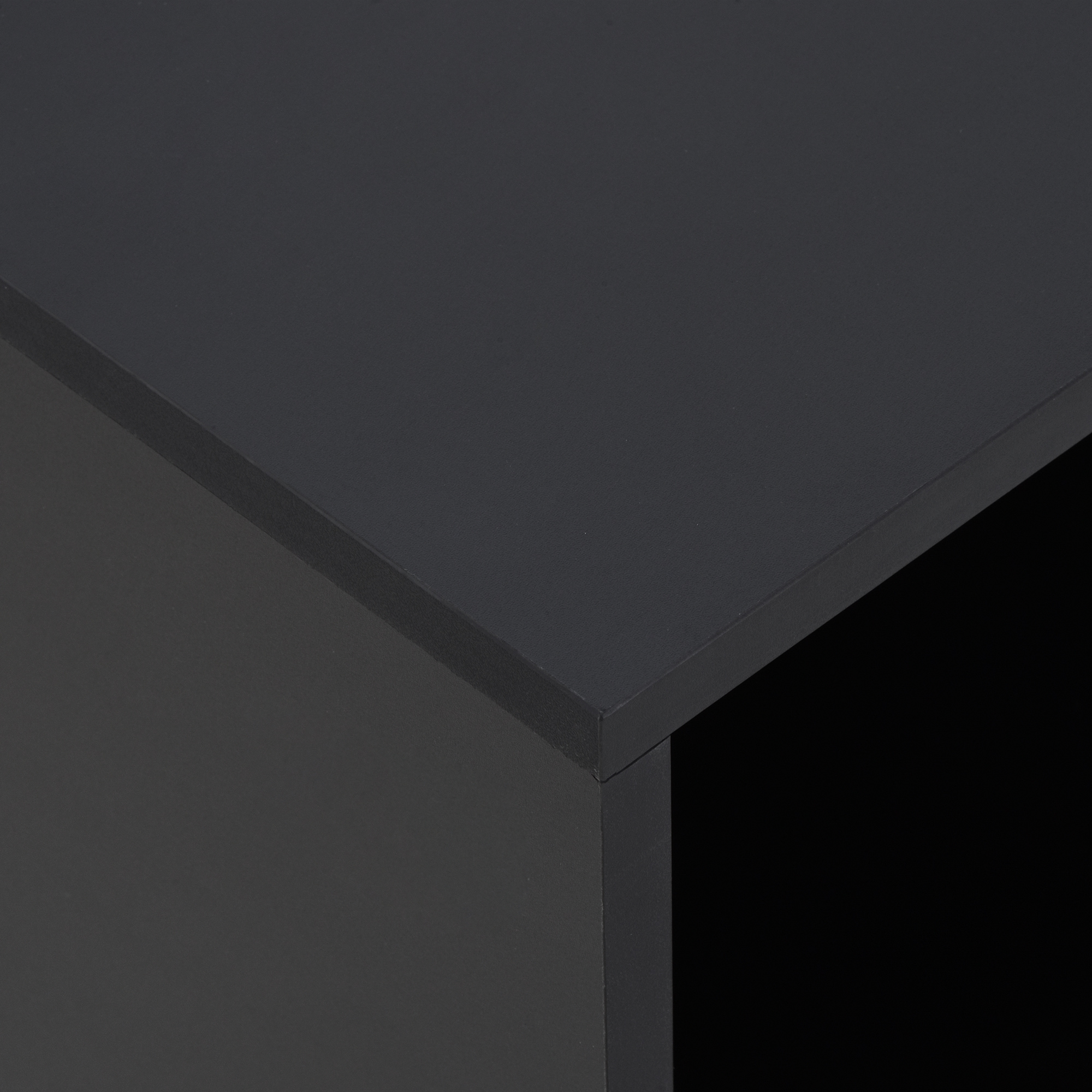Primo piano di una superficie angolare grigio scuro con finitura strutturata, il bordo di un cubo, con sfondo nero.