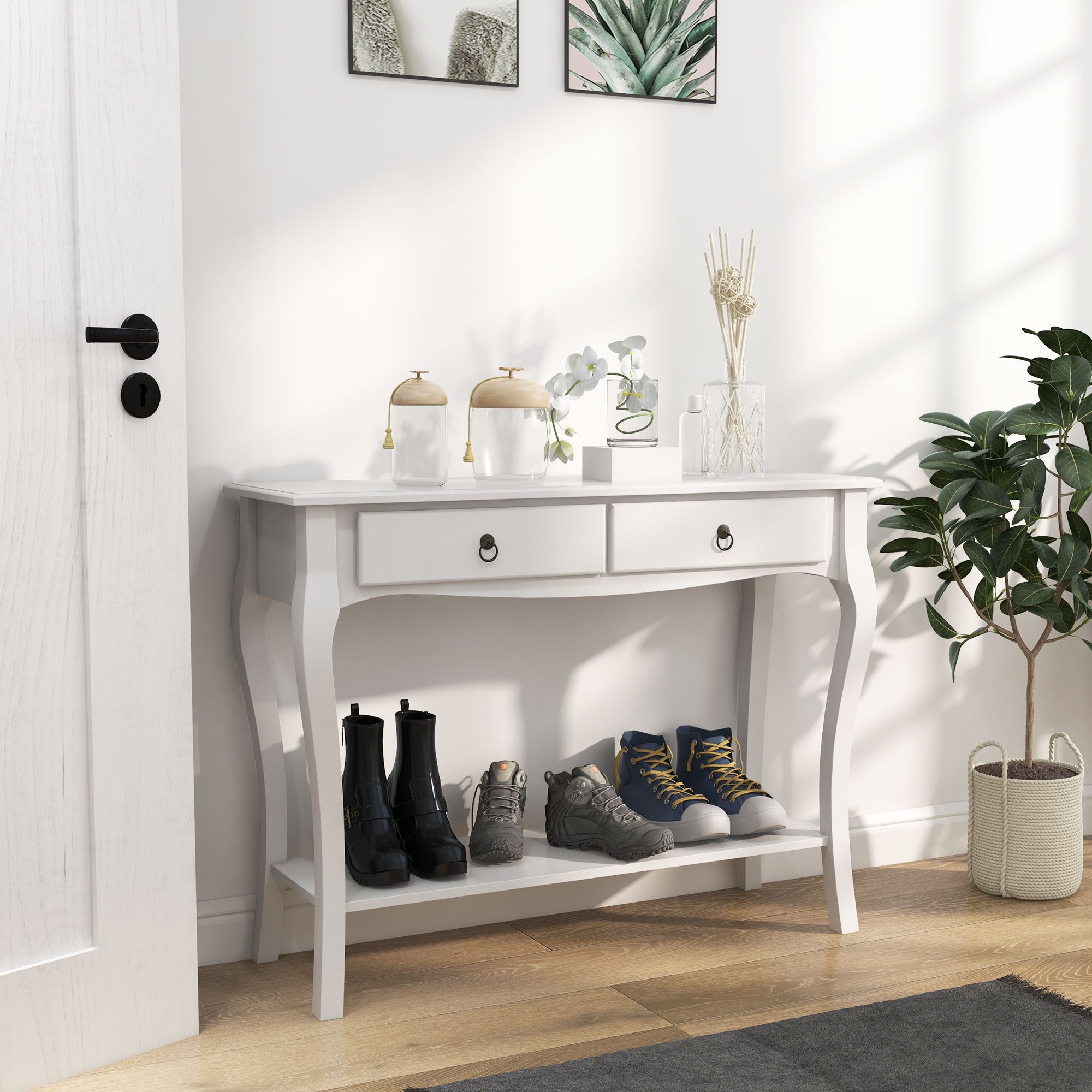 Tavolo da ingresso bianco con due cassetti. Stivali neri, scarpe da ginnastica e scarpe sullo scaffale. Muro con immagini e porta.