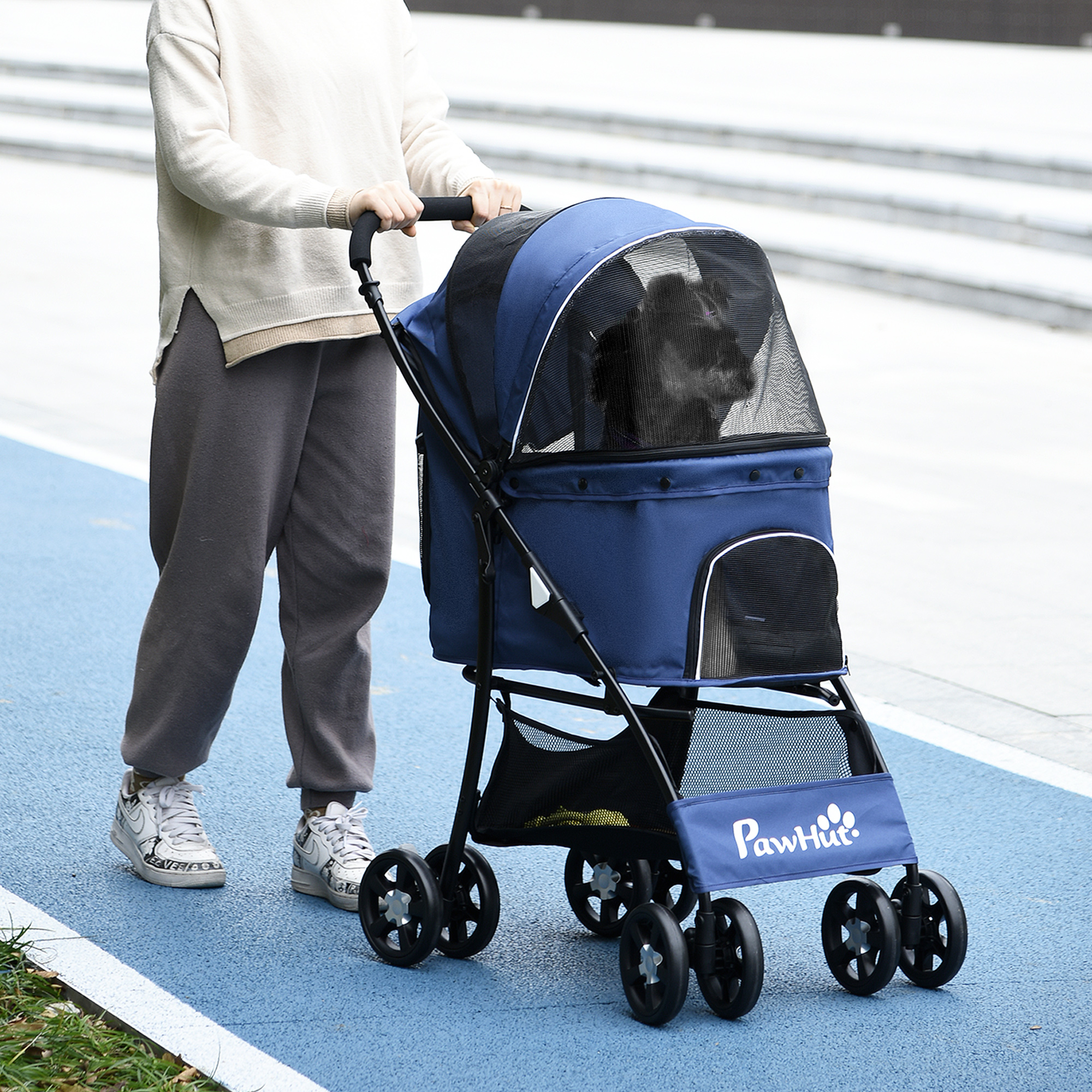 Una persona spinge un passeggino blu per animali domestici con un cane all'interno su una superficie blu.
