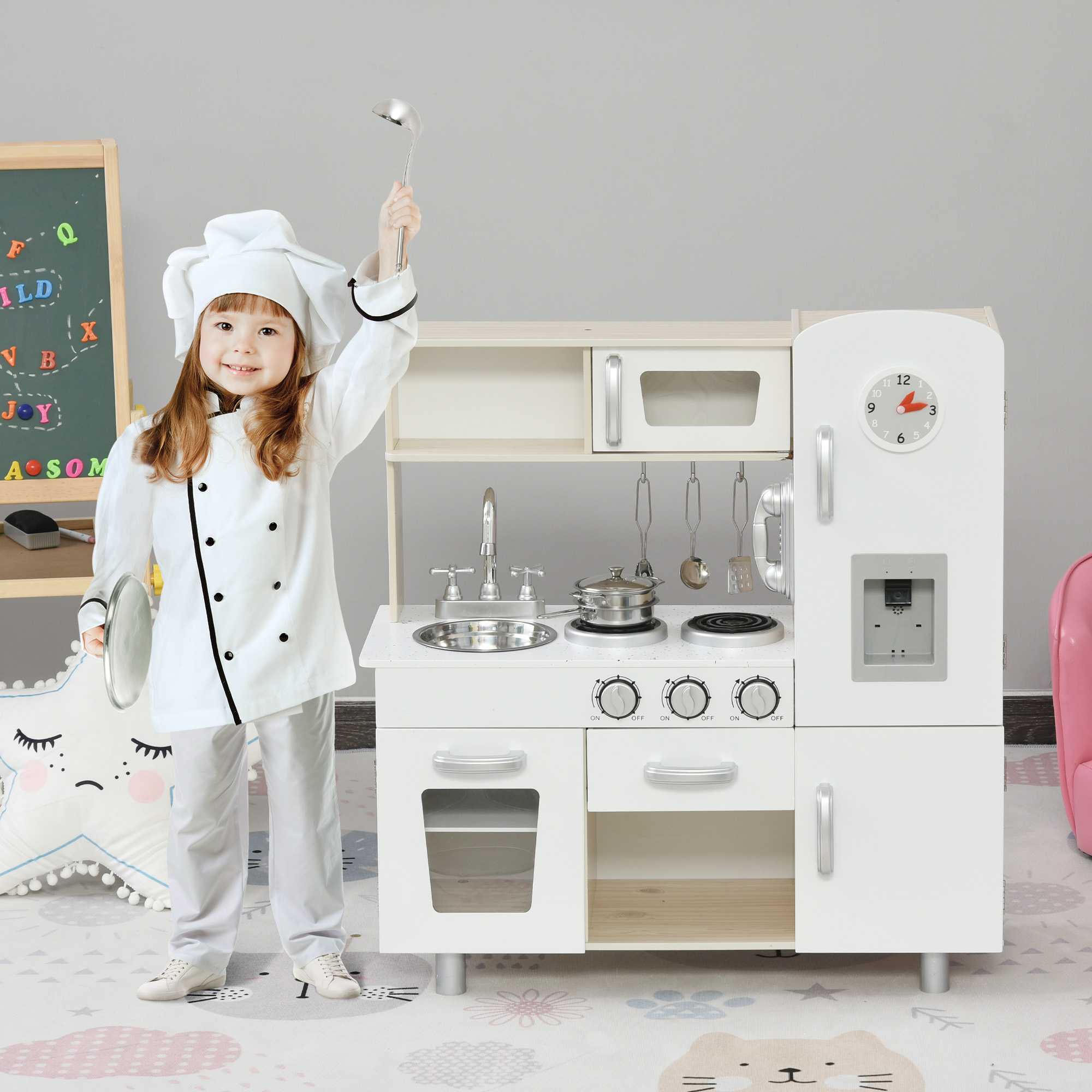 Ragazza con abito da chef con set da cucina giocattolo. La cucina comprende orologio, fornello e frigorifero.