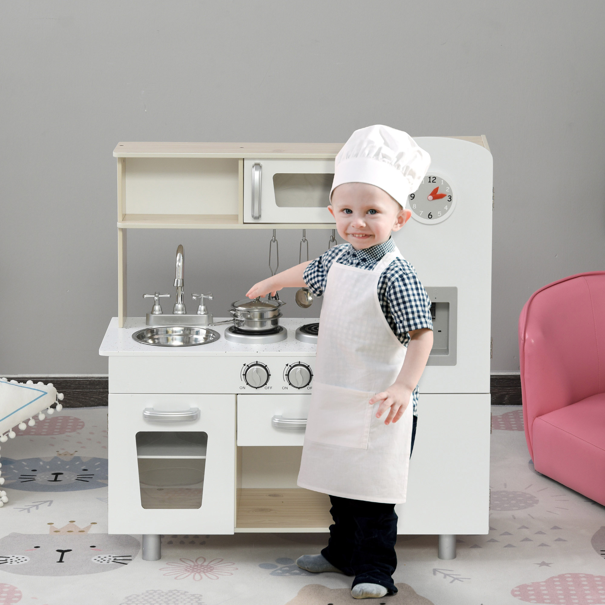 Bambino piccolo con cappello e grembiule da chef che gioca con una cucina giocattolo.