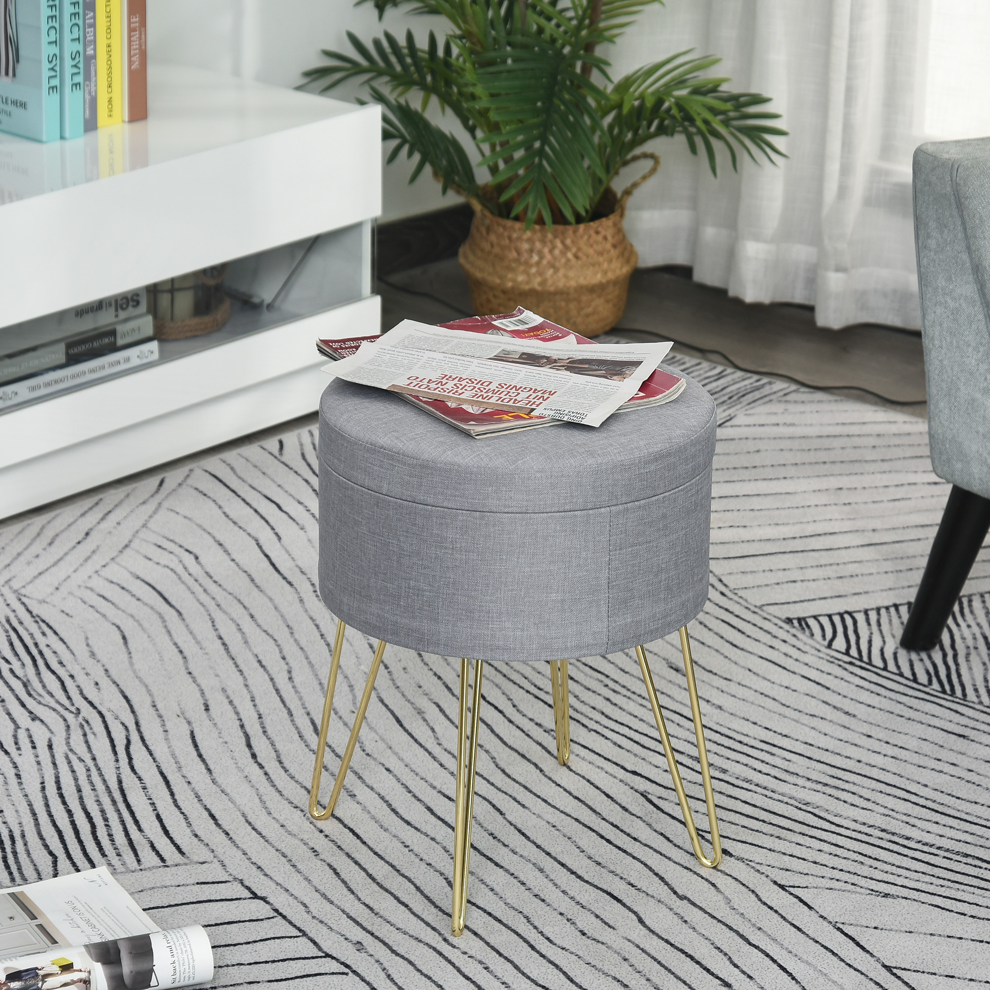 Un pouf in tessuto grigio con gambe dorate. Un giornale è appoggiato sopra il pouf.