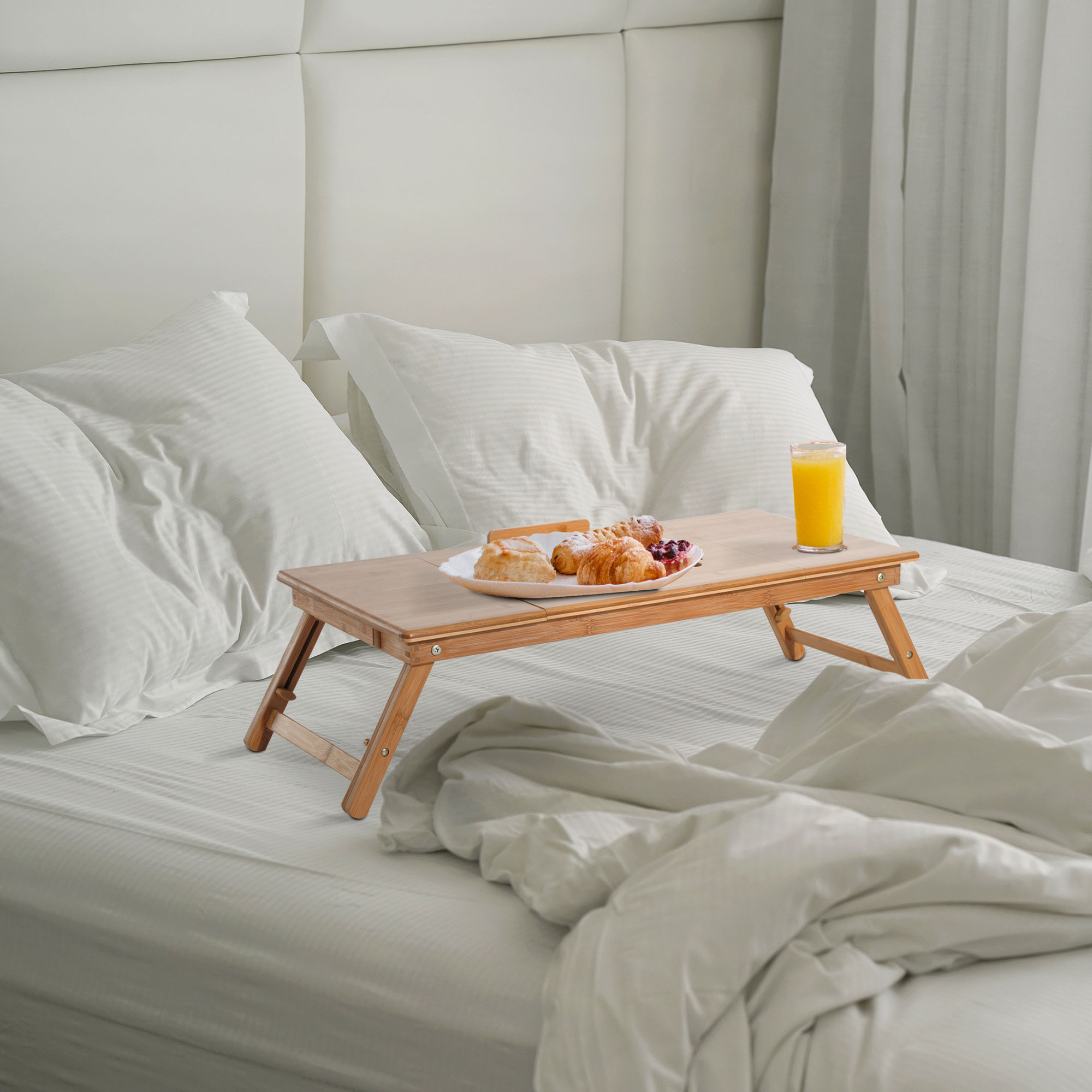 Colazione a letto: vassoio con cibo e bevande su un letto con cuscini e piumino bianco.