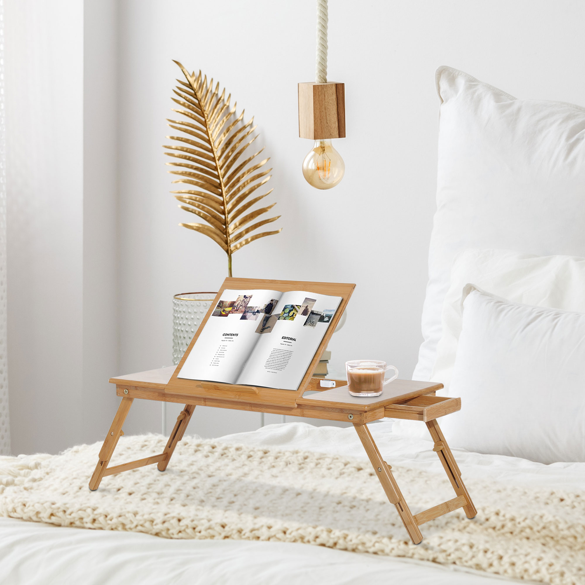 Un vassoio da letto in legno con un libro, una tazza e una lampada su un letto.