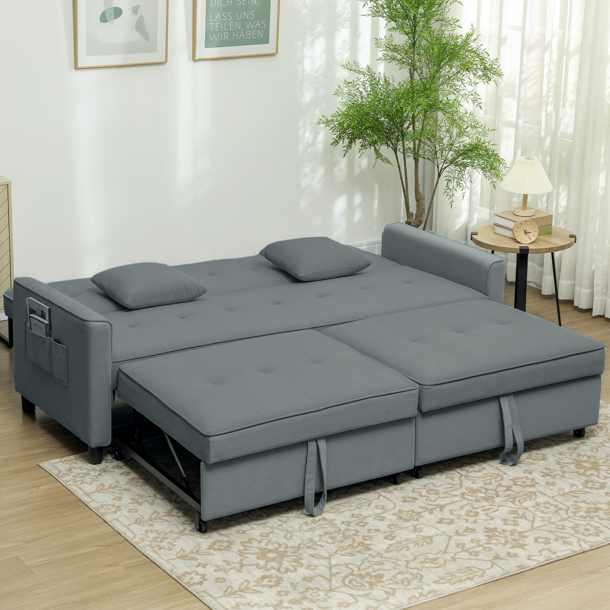 Divano letto grigio con due cuscini e una sezione estraibile. È su un tappeto fantasia con un albero.