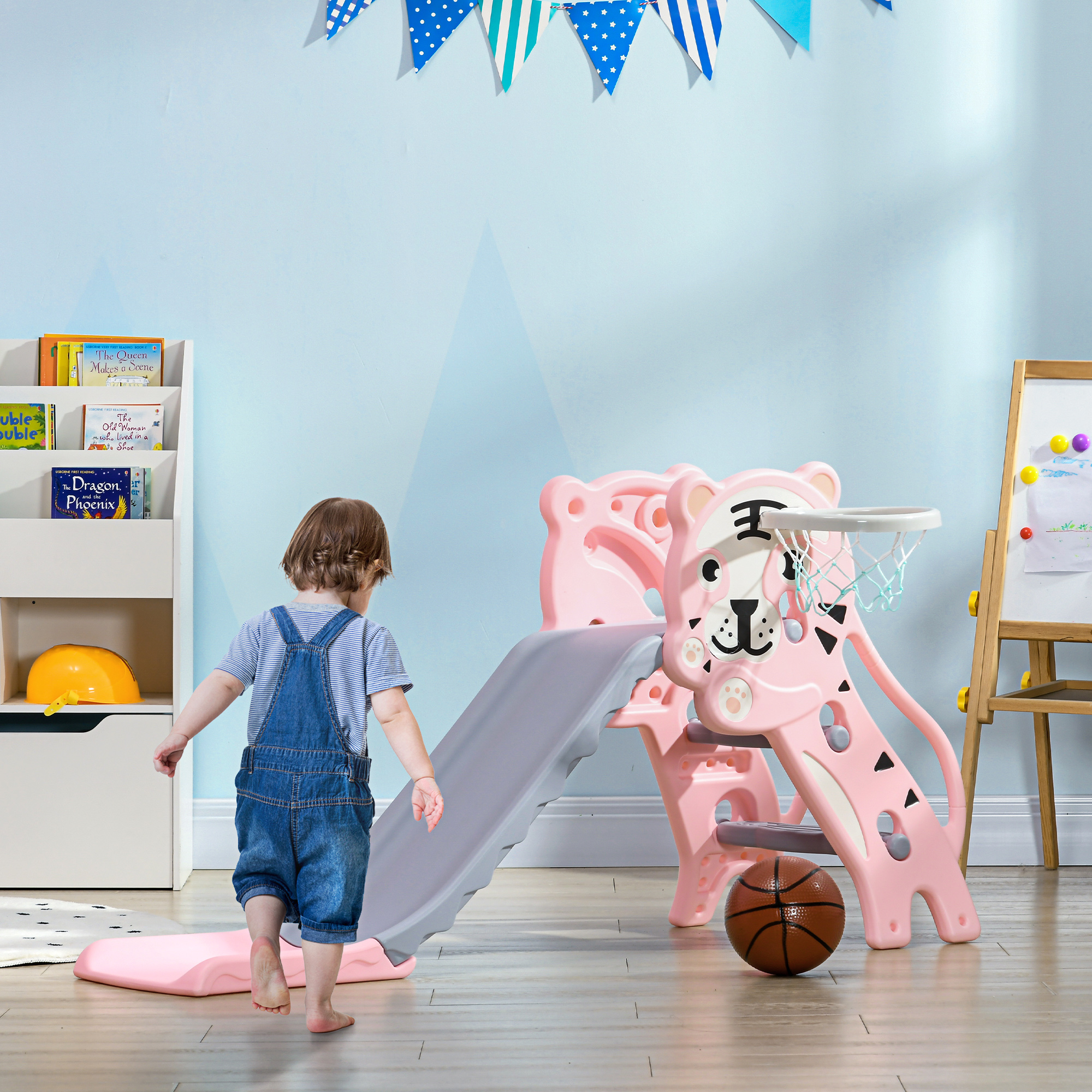 Un bambino cammina verso uno scivolo rosa con un canestro da basket. Ci sono libri e giocattoli nella stanza.