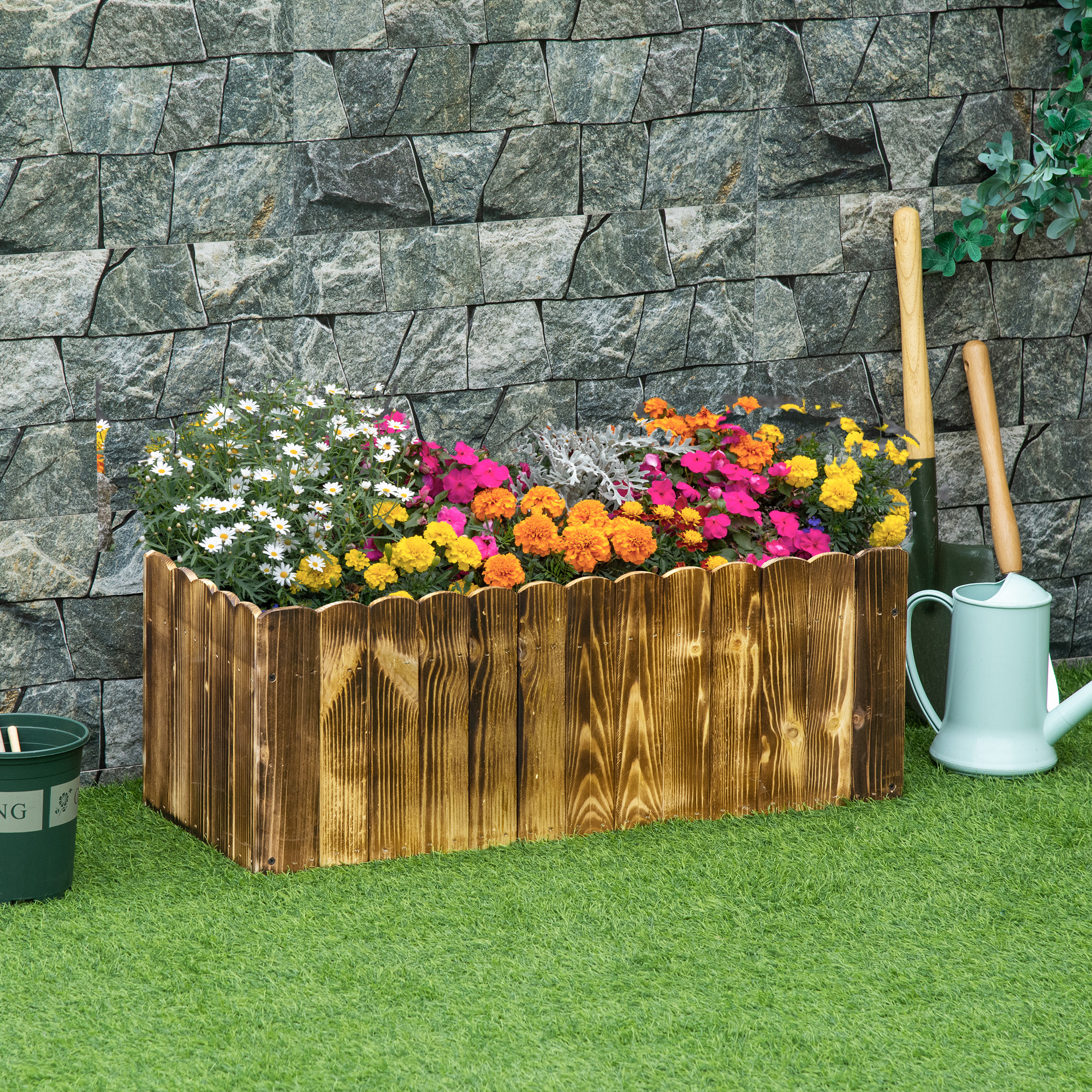 Una fioriera in legno con fiori colorati e uno sfondo di muro di pietra, attrezzi e un annaffiatoio.