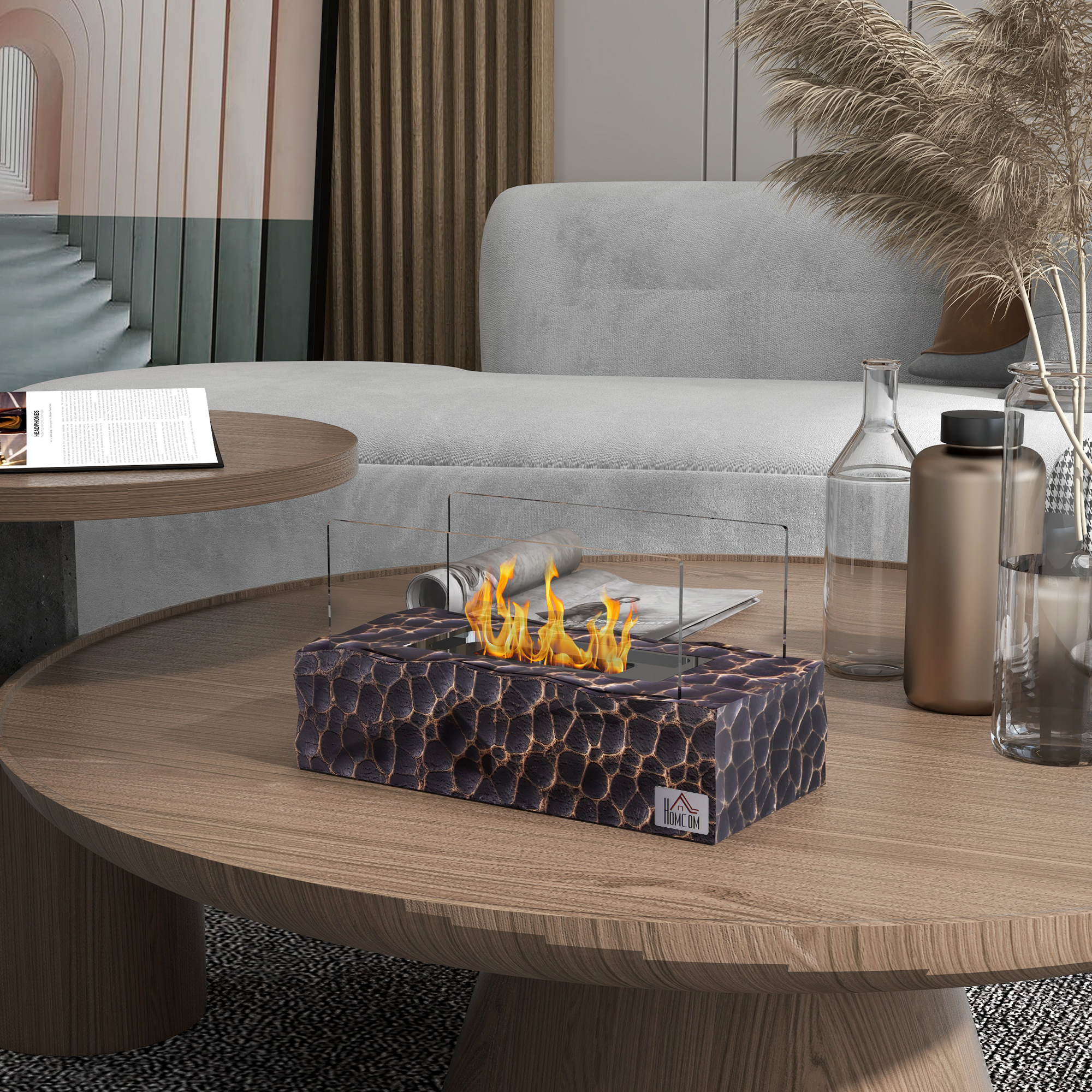 Caminetto moderno con base decorata, involucro in vetro e fiamme visibili su un tavolo.