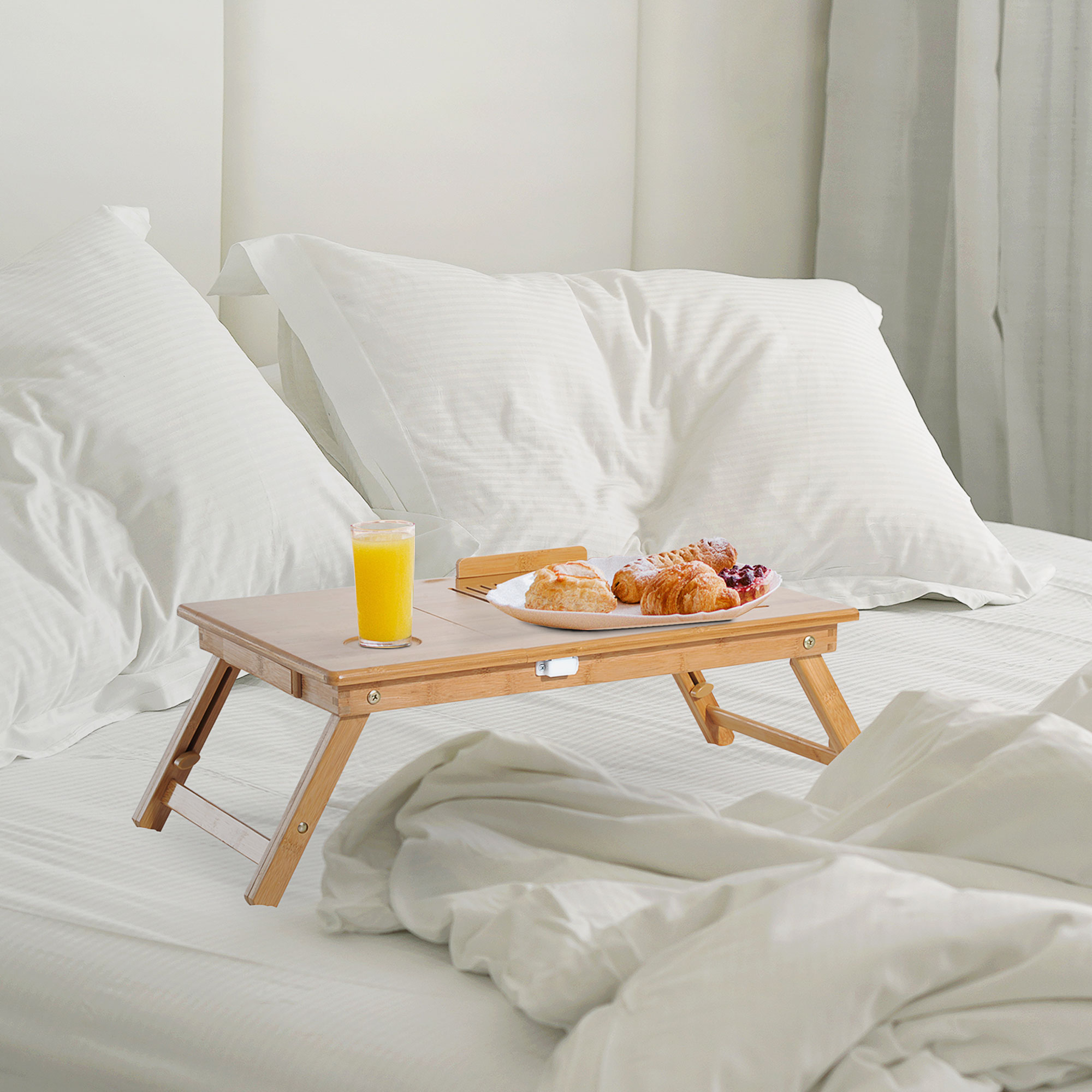 Bandeja de cama de bambú con comida y jugo, sobre una cama con sábanas blancas.