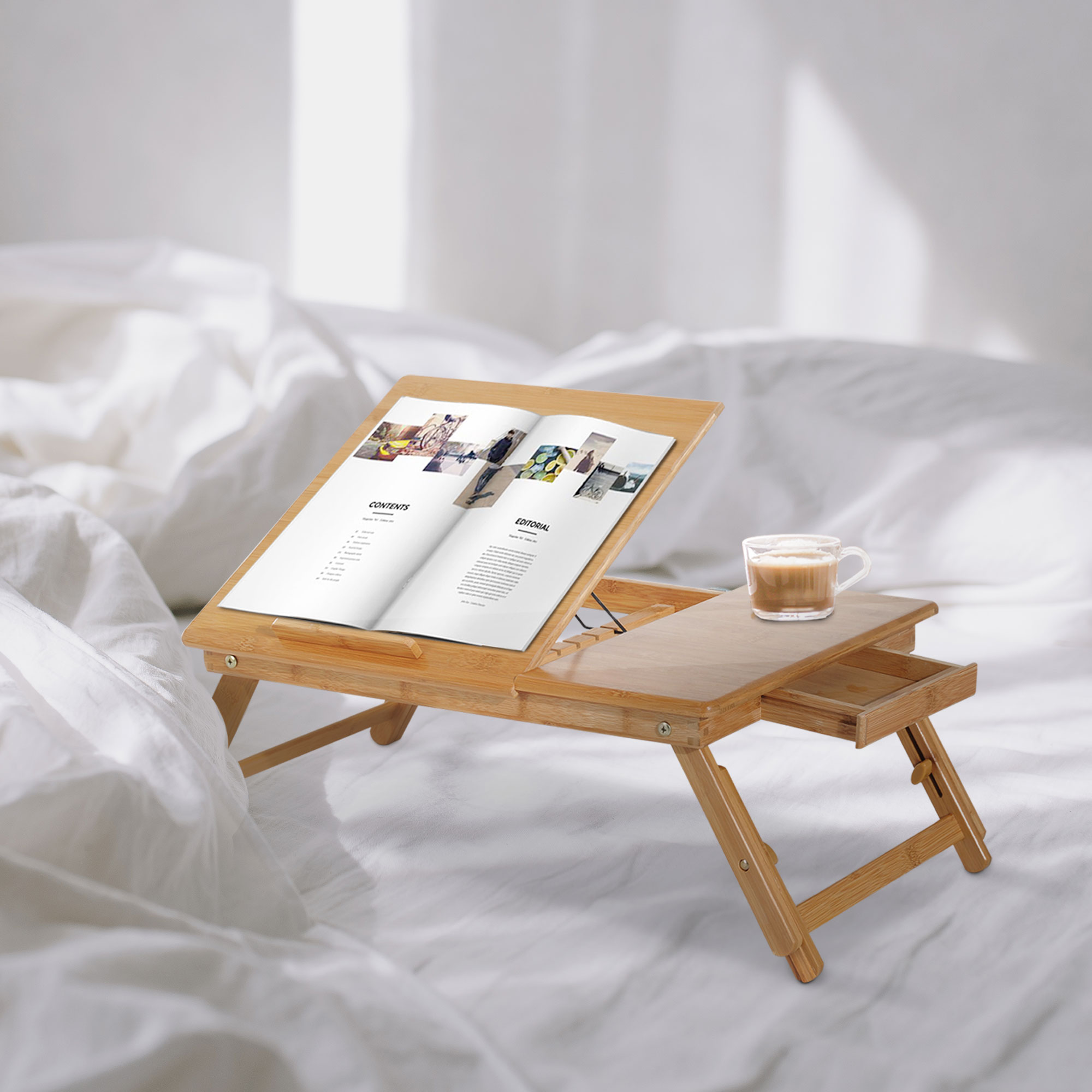 Scrivania da letto in bambù con libro aperto e caffè su un letto con lenzuola bianche.