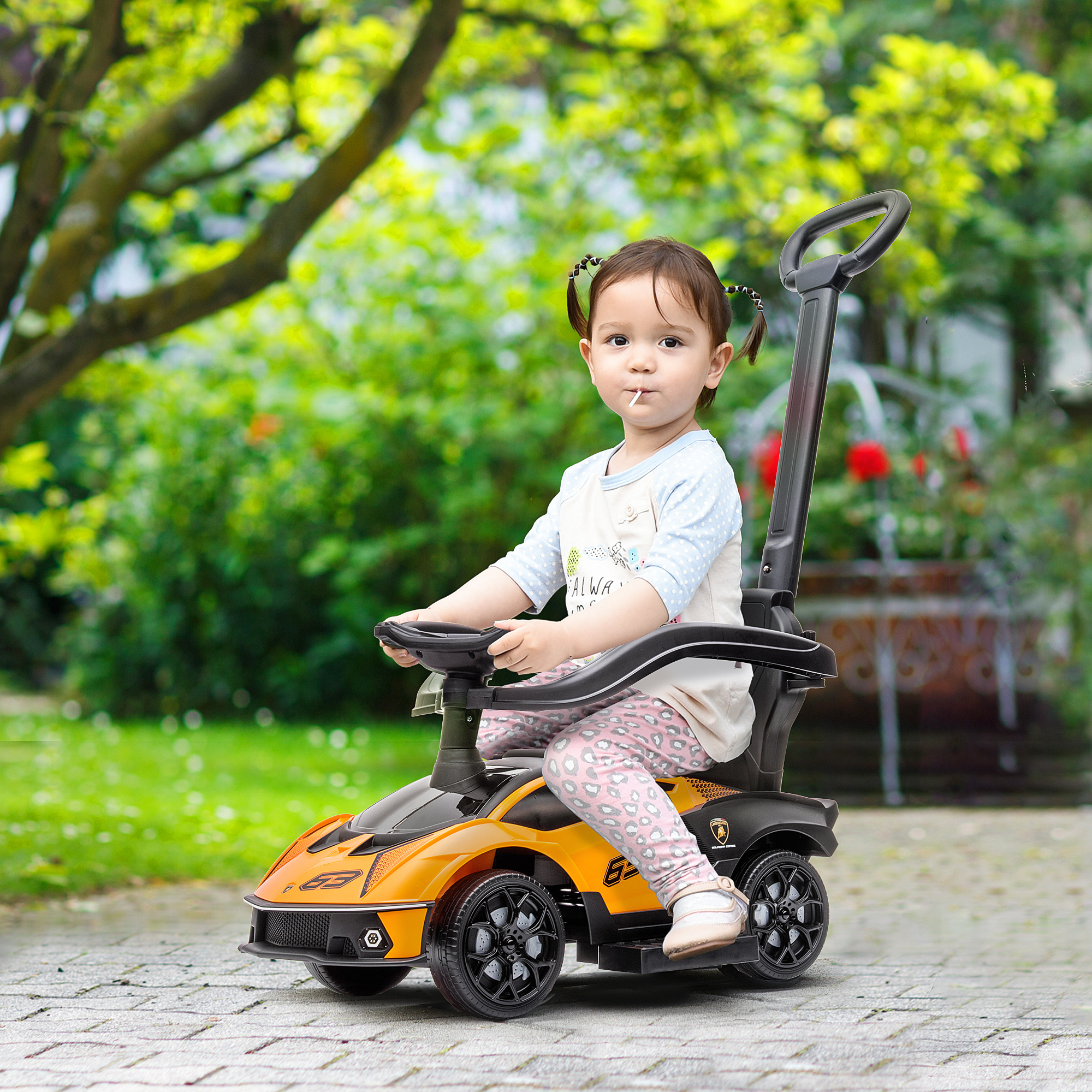 Un bambino piccolo è seduto in un'auto giocattolo gialla e nera e tiene in mano un lecca-lecca.