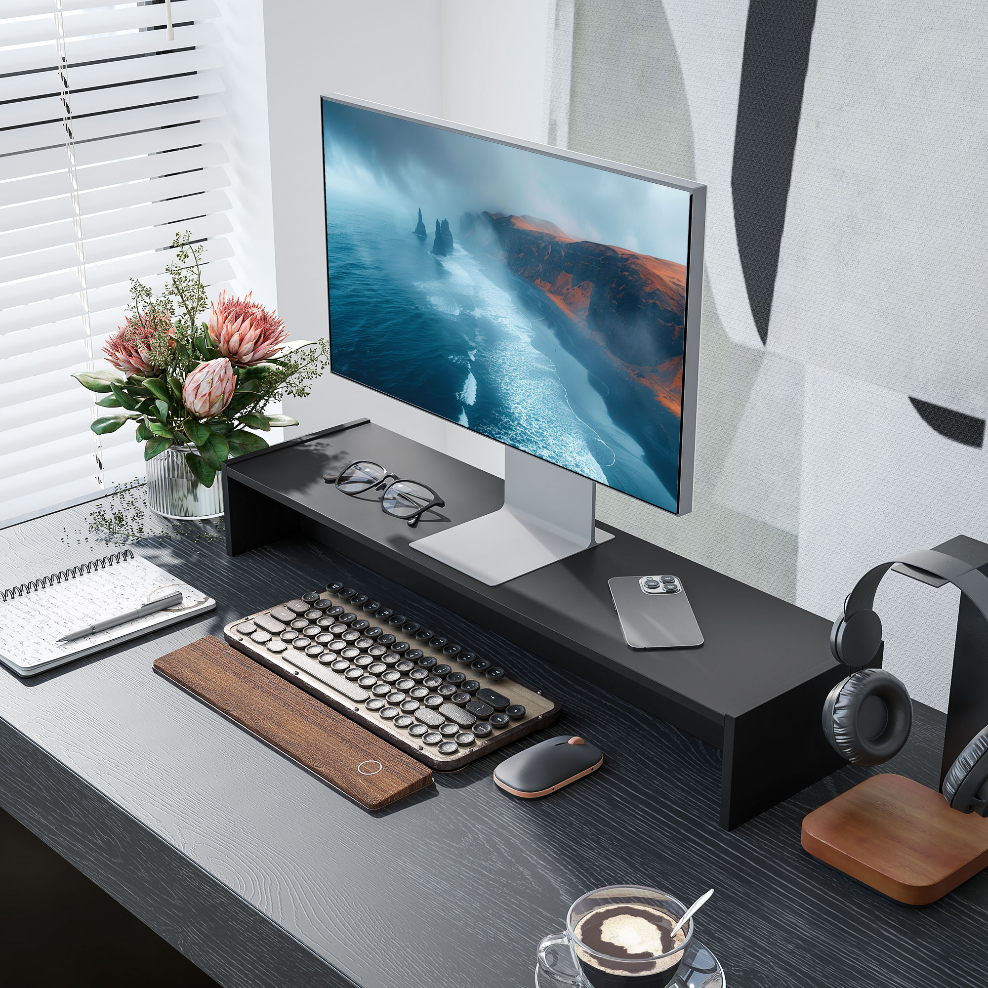 Un setup da scrivania con monitor, tastiera, mouse e cuffie. Sono presenti fiori e una tazza di caffè.