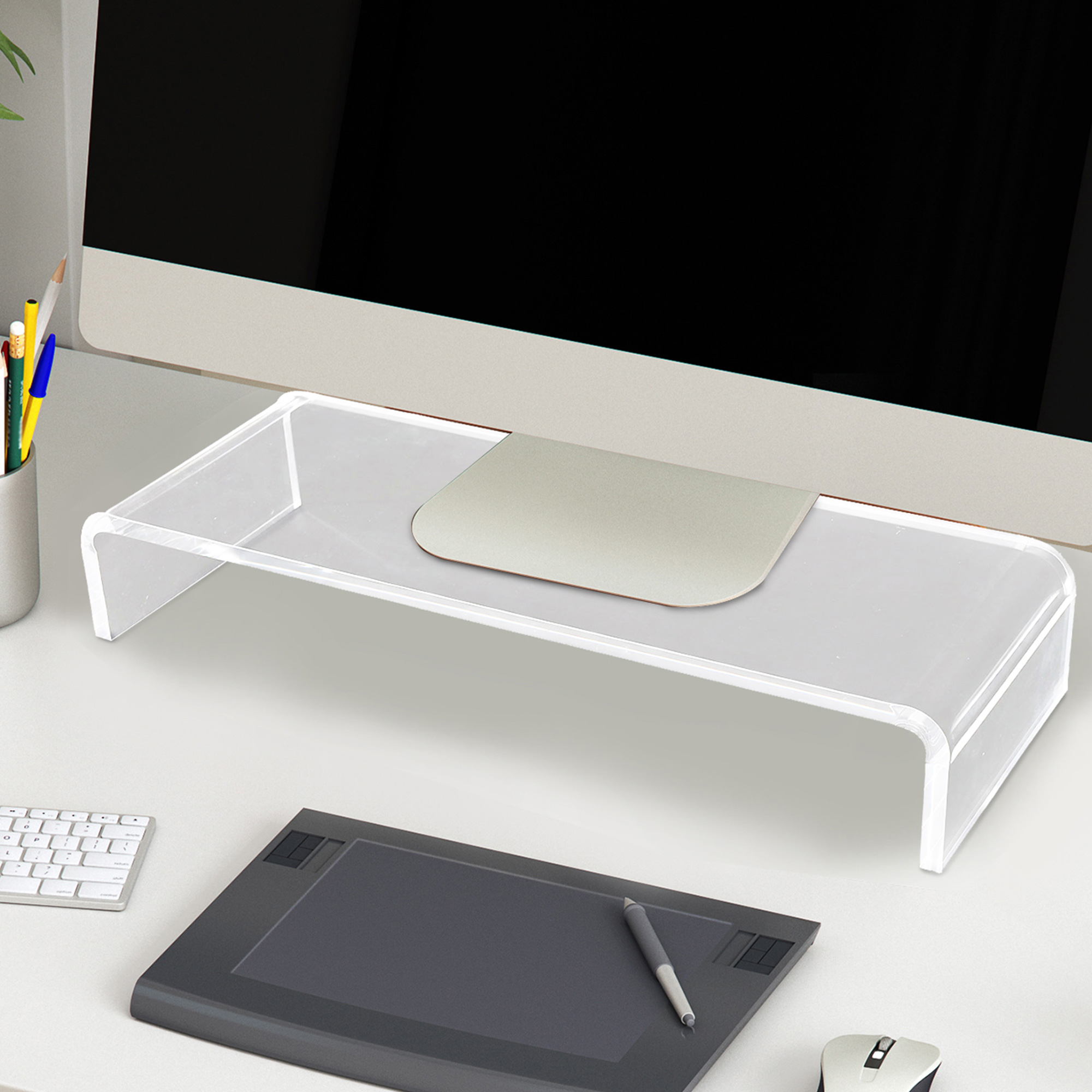 Supporto per monitor in acrilico su scrivania bianca. Tastiera, mouse e penna visibili.