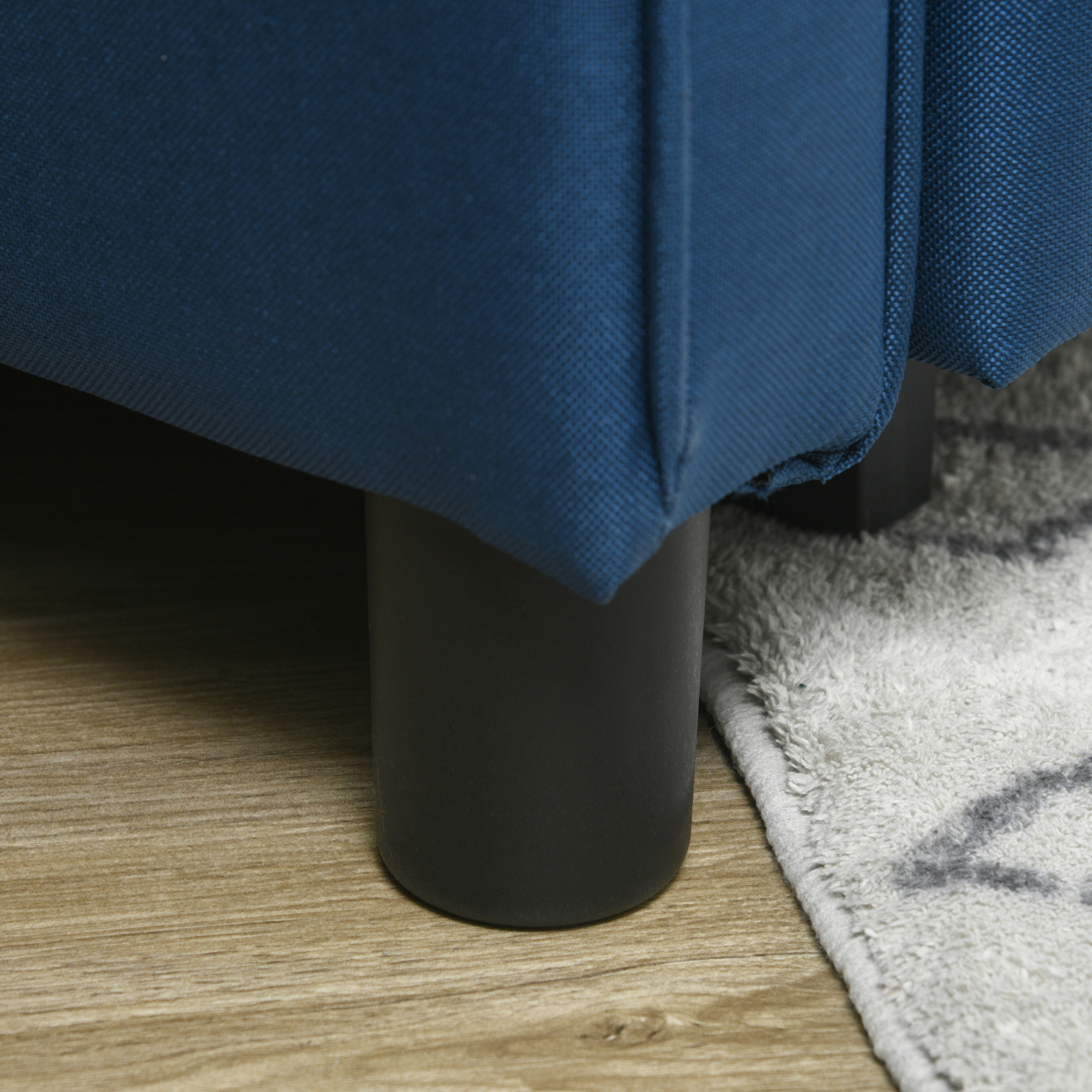 Piedino del divano blu su pavimento in legno. Un tappeto è parzialmente visibile.