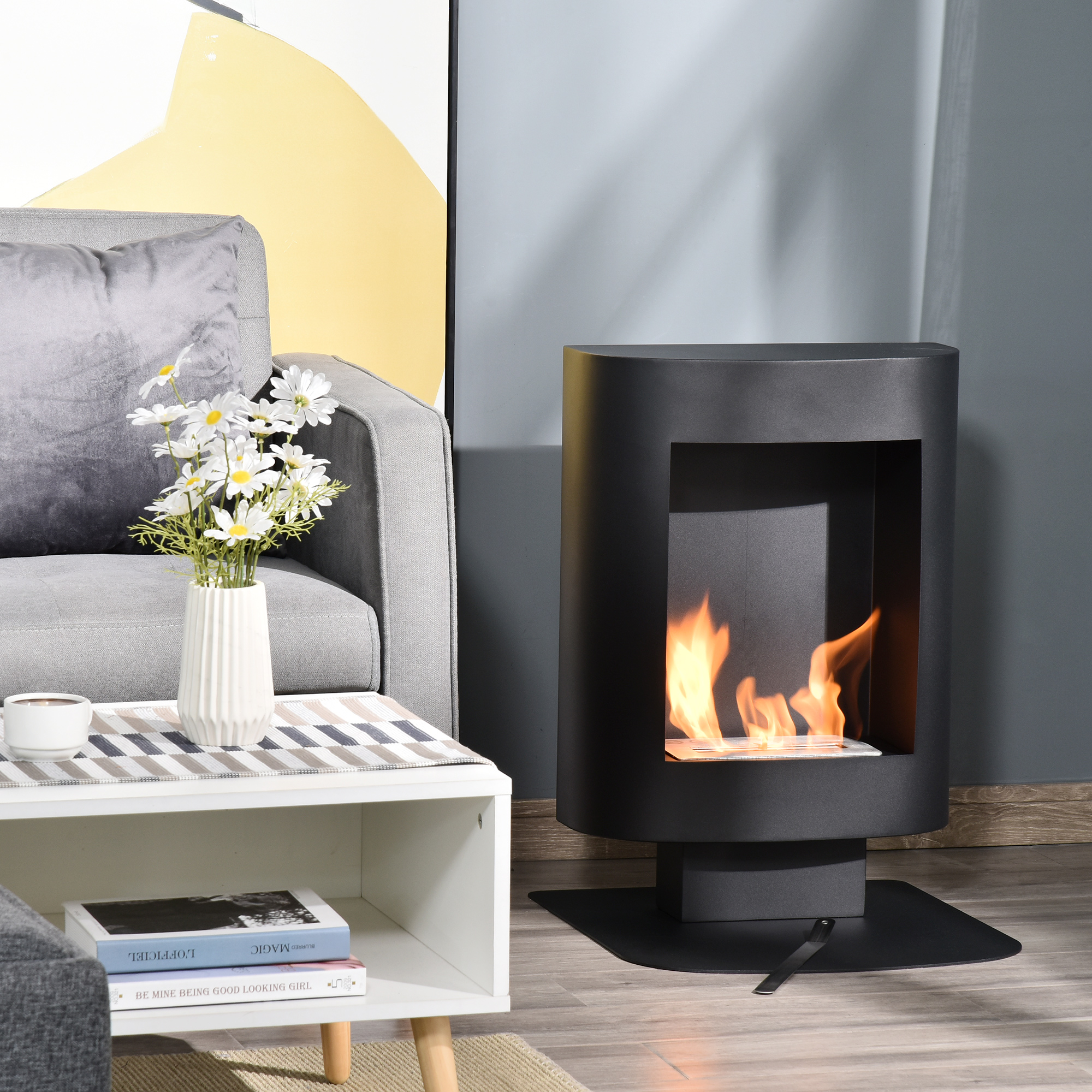 Un caminetto nero con fiamme è in una stanza accanto a un divano, un tavolo e un vaso con fiori.