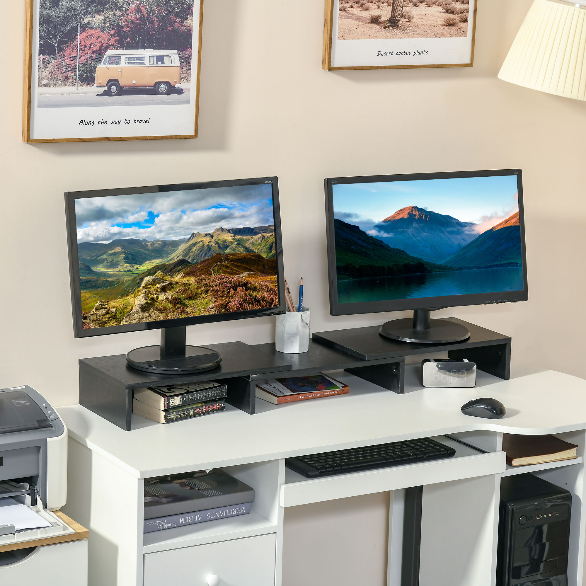 Una scrivania con due monitor che mostrano paesaggi. Ci sono libri, una tastiera e un computer. L'arte è appesa al muro.