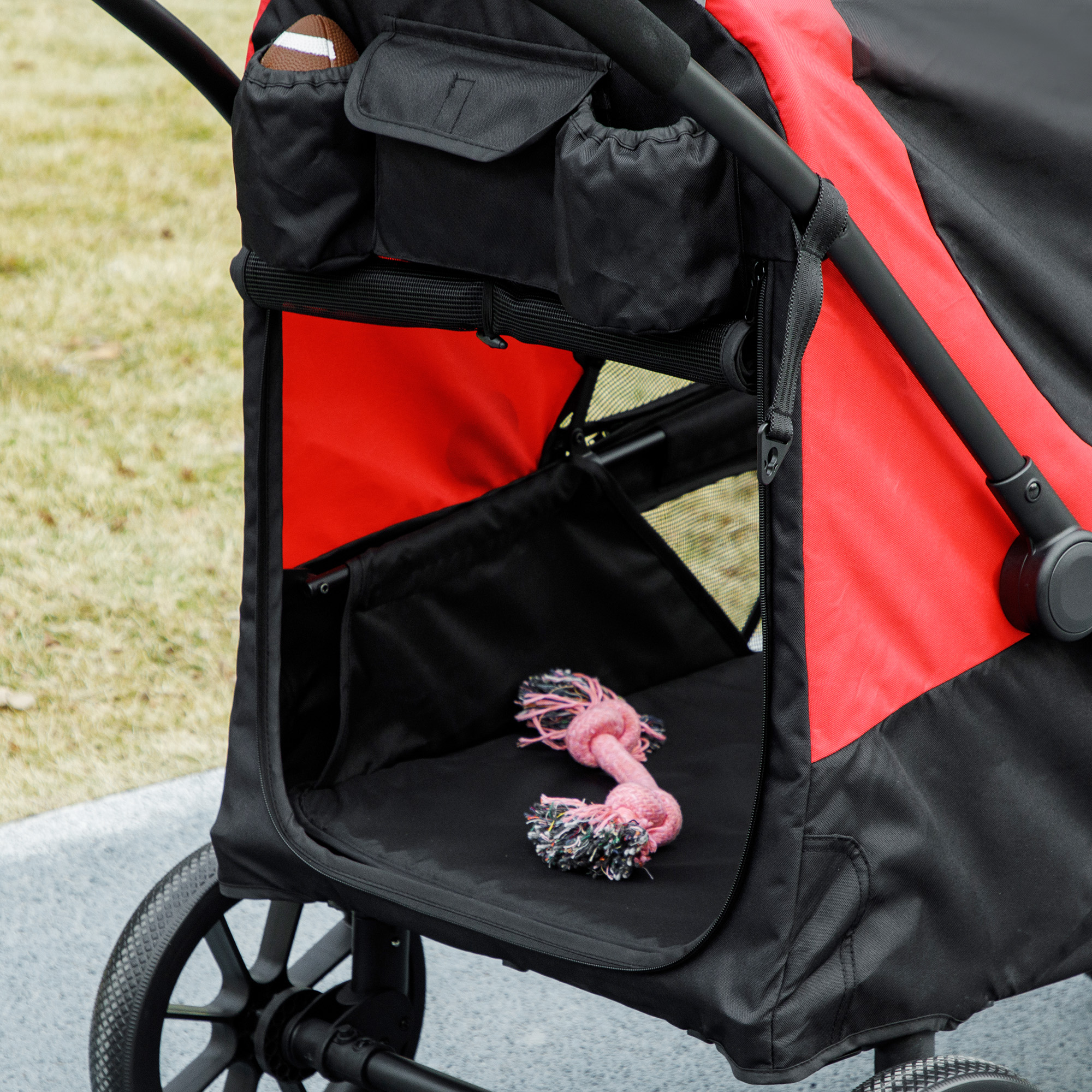 Un carrello per animali nero e rosso con un giocattolo rosa nella parte anteriore. Il carrello è su un marciapiede.