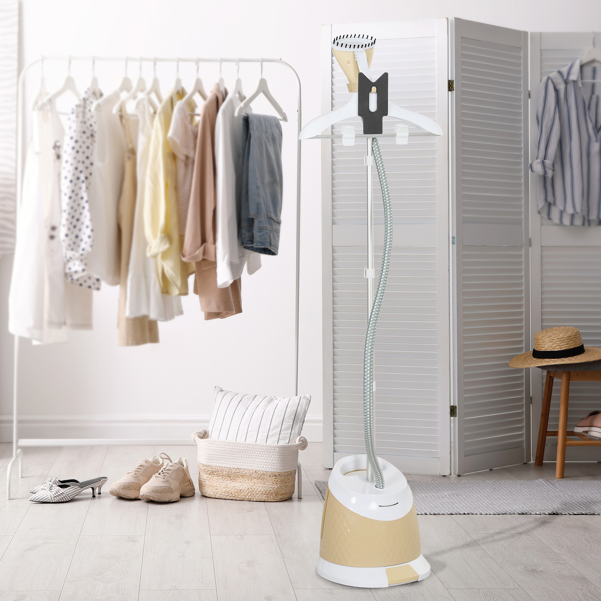 Un vaporizzatore per vestiti e vestiti su un rack. Scarpe e un cuscino sono sul pavimento. Un paravento è dietro.
