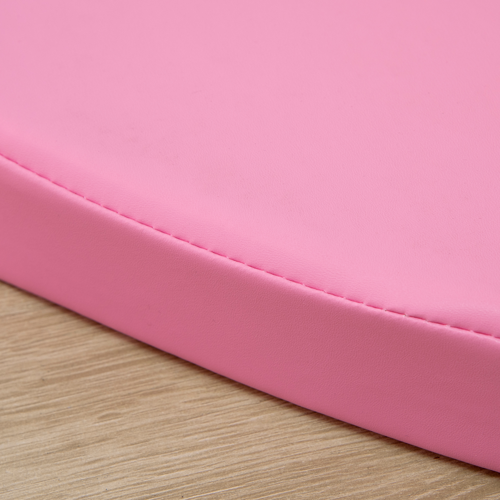 Primo piano di un cuscino rosa, arrotondato. Il bordo del cuscino è su una superficie in legno.