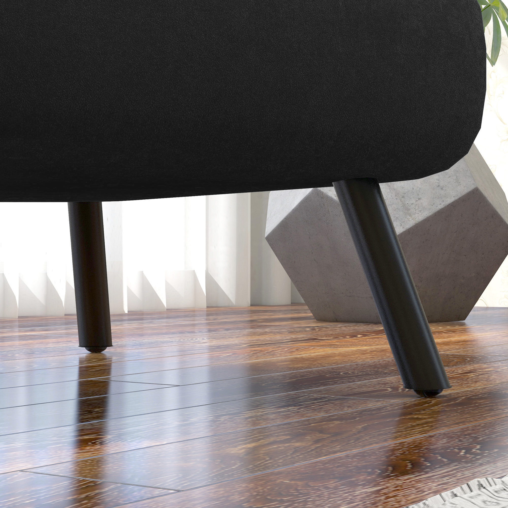 Primo piano di gambe di sedia nere su pavimento in legno, con blocco di cemento geometrico.