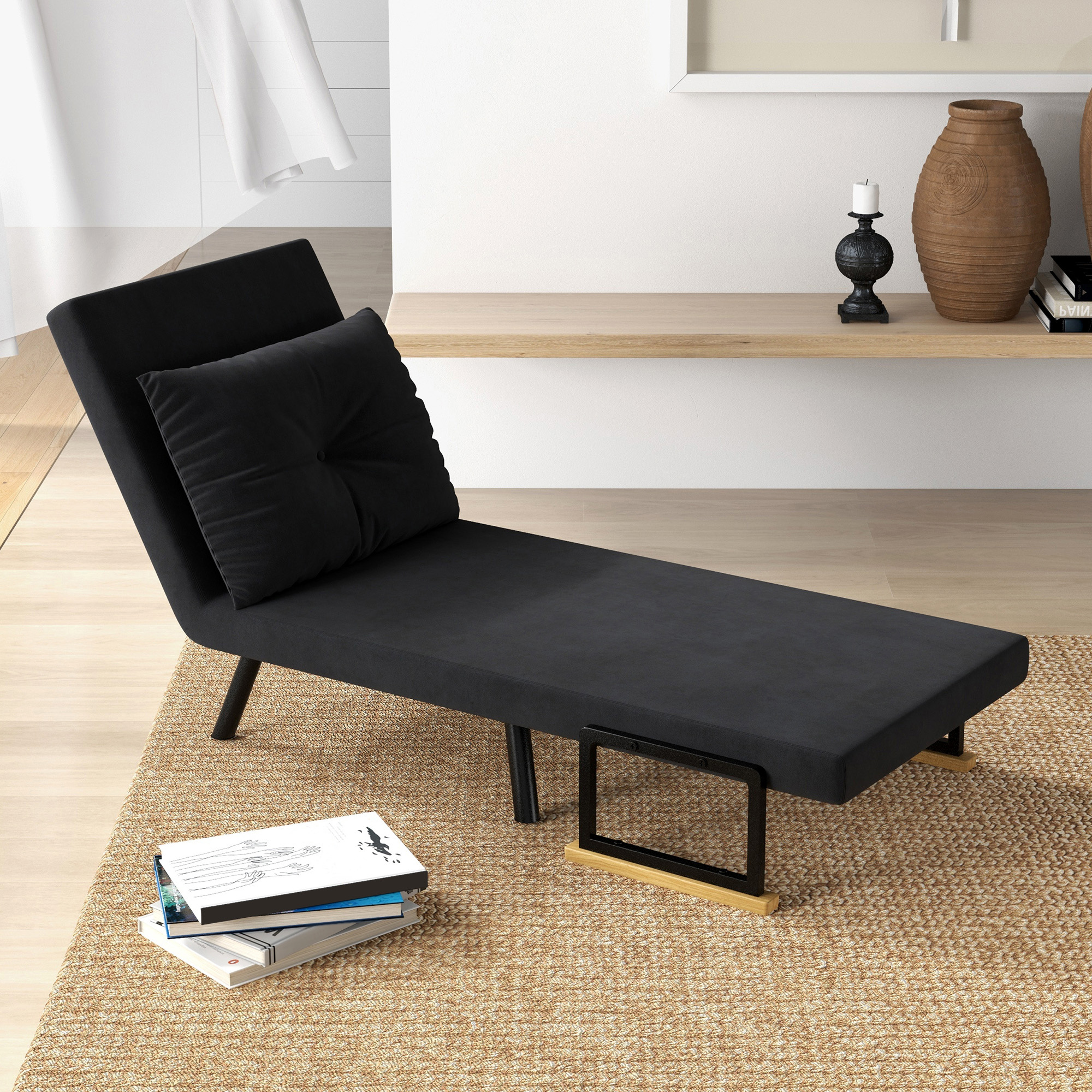 Una chaise longue nera con un cuscino nero. Ci sono libri e decorazioni nelle vicinanze.