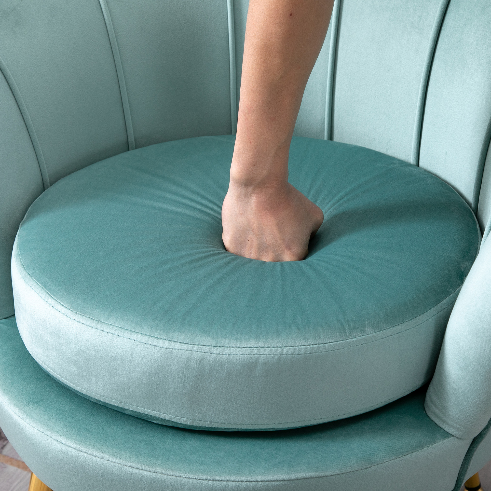 Mano che preme su una seduta imbottita, color teal. La sedia ha gambe dorate.