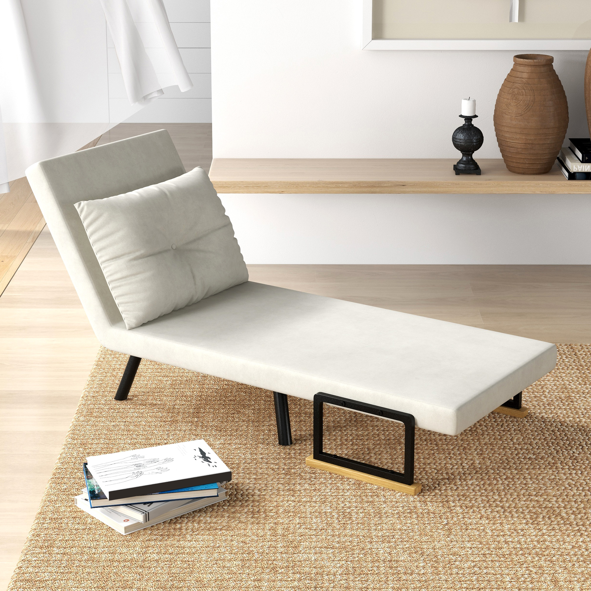 Una chaise longue bianca con gambe nere e un cuscino. Libri e una cornice sono nelle vicinanze.
