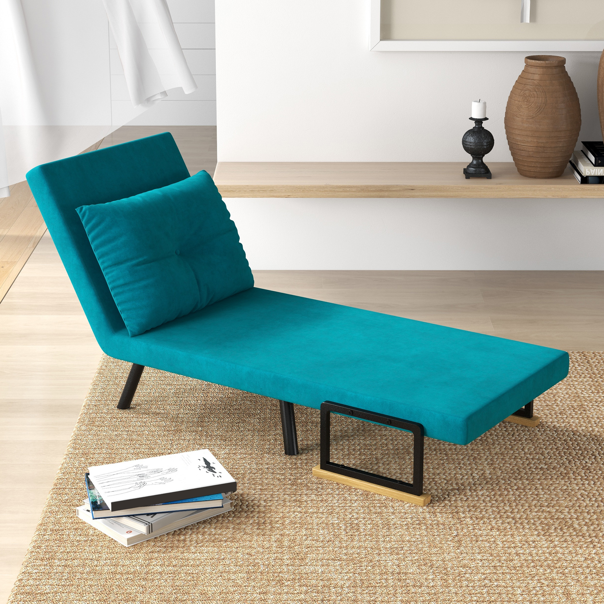 Chaise longue turchese con cuscino, su un tappeto. Libri e oggetti decorativi. Parete bianca sullo sfondo.