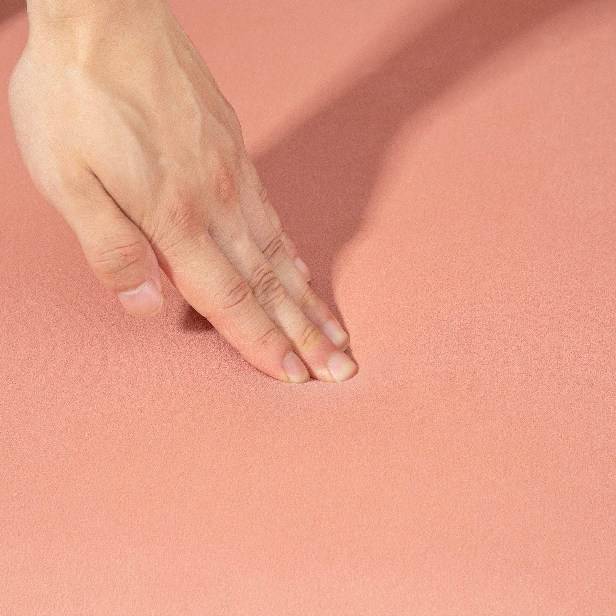 Mano che tocca una superficie rosa. Tono della pelle visibile. La superficie sembra morbida.