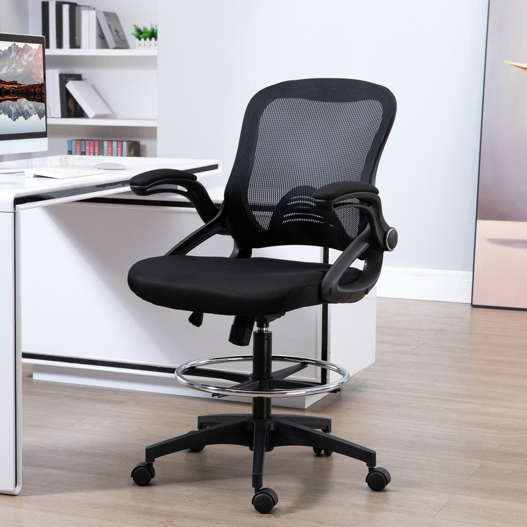 Una sedia da ufficio in rete nera con poggiapiedi è di fronte a una scrivania bianca e un computer.