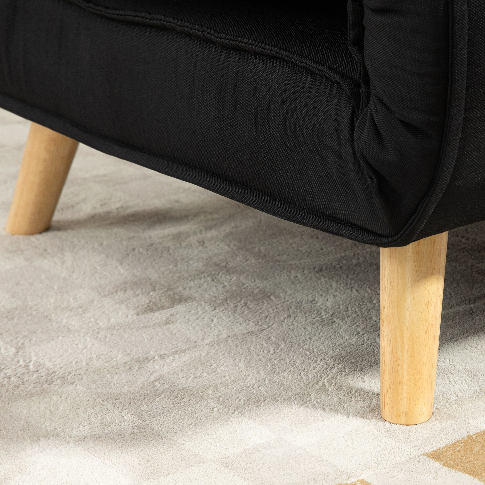 Nahaufnahme des Beins eines schwarzen Sofas auf einem gemusterten Teppich. Das Bein ist helles Holz.