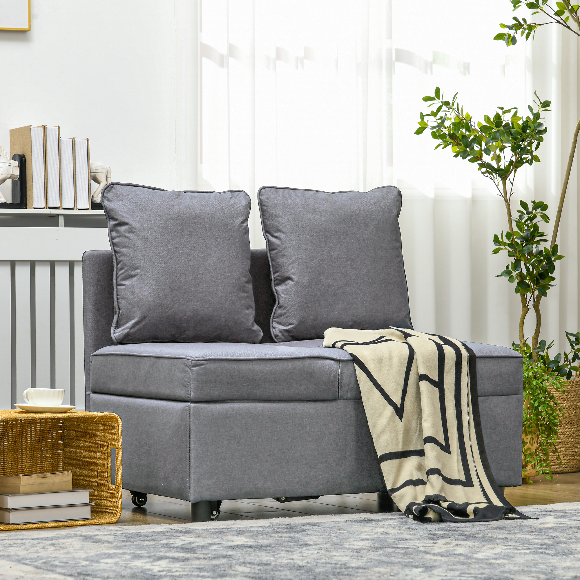 Divano modulare grigio con due cuscini e una coperta. Su rotelle, su un tappeto.