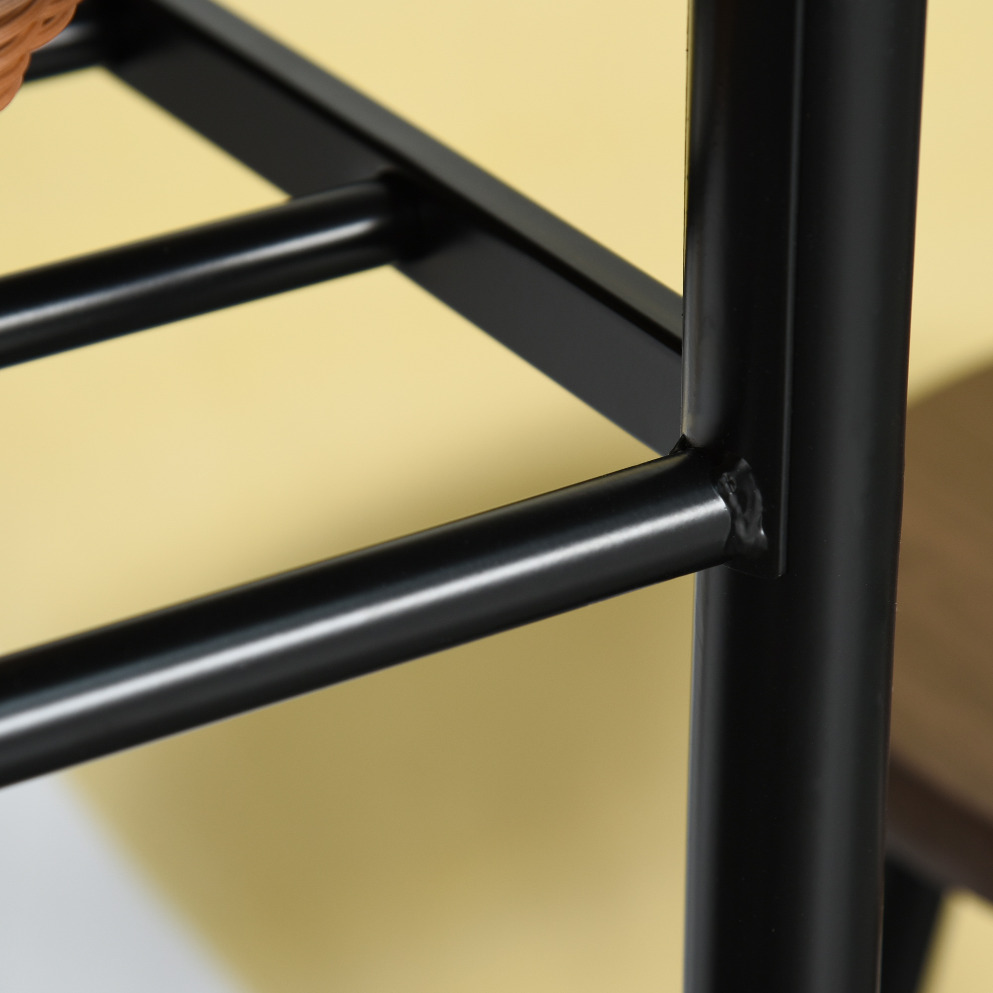 Primo piano di un telaio in metallo nero con giunti saldati, su sfondo giallo.