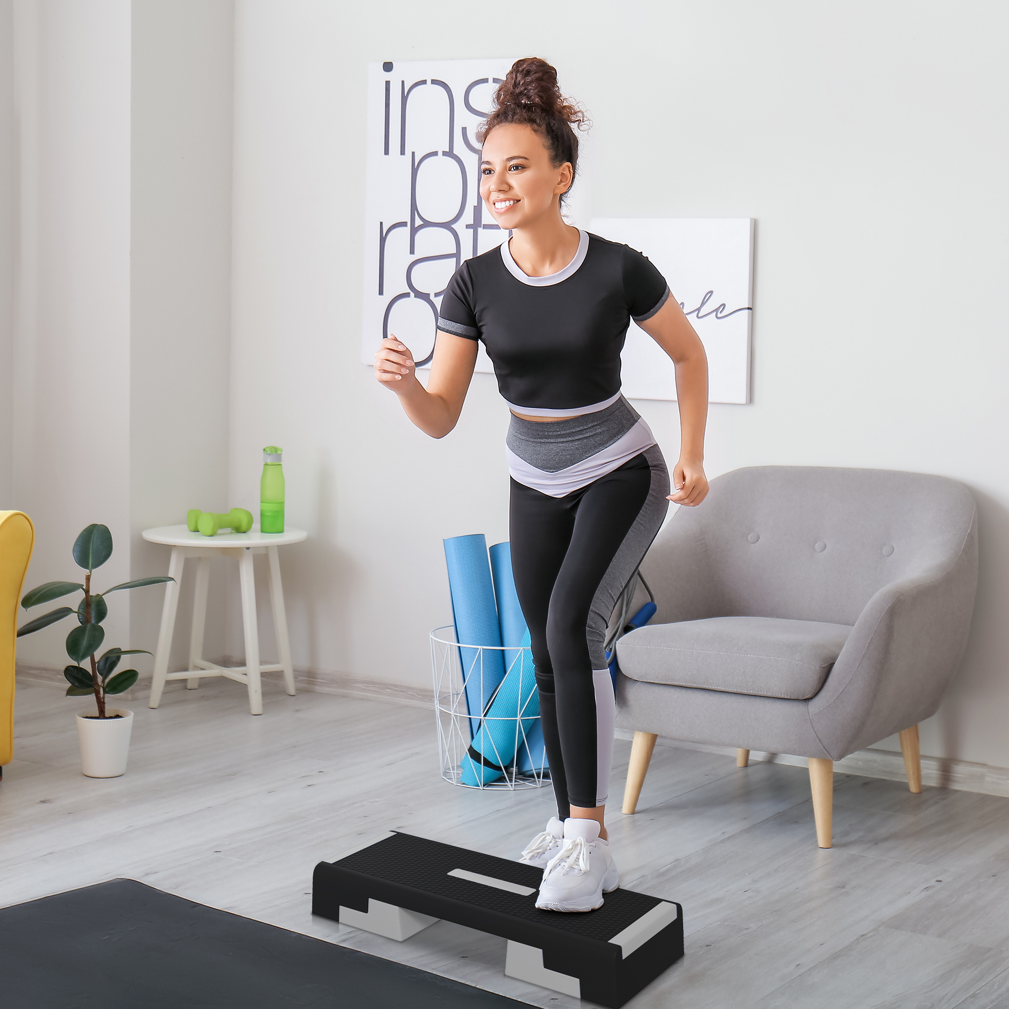 Donna che si esercita su una piattaforma di step nera in palestra domestica, in abbigliamento sportivo, sorridente.