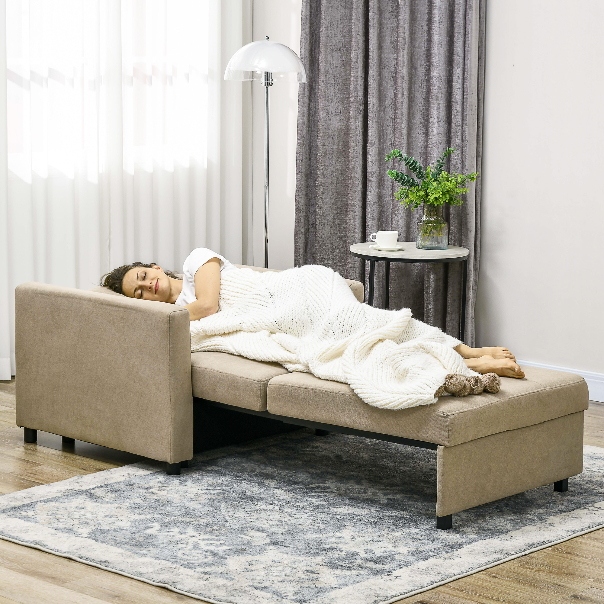 Donna che dorme su un divano letto beige, coperta da una coperta bianca, in una stanza con un tappeto.