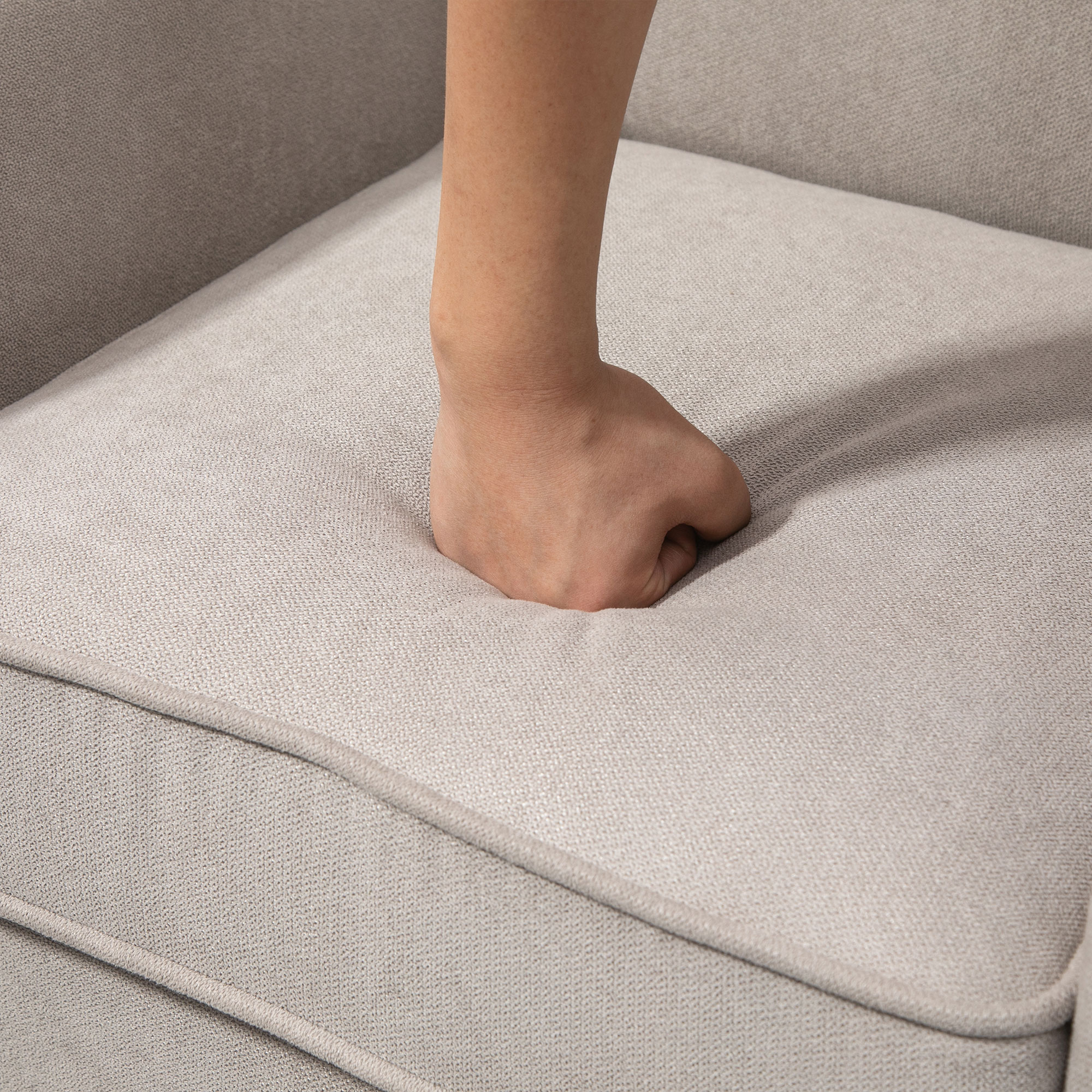 Una mano che preme su un tessuto grigio chiaro. Il tessuto mostra una leggera rientranza.