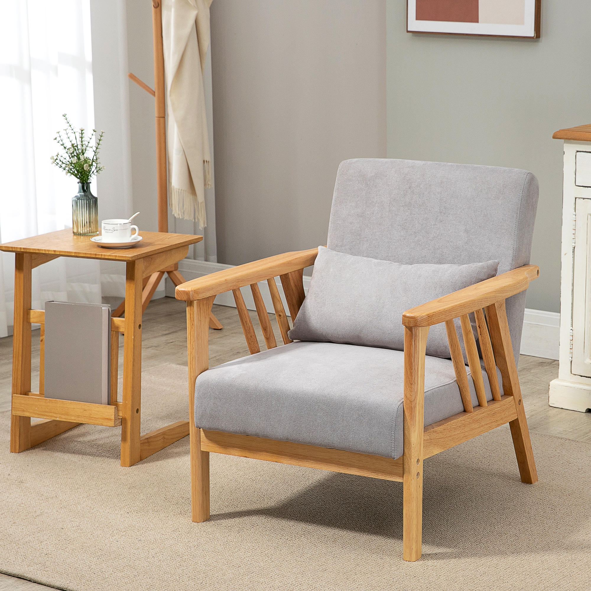 Poltrona grigia con struttura in legno, tavolino con vaso e tappeto beige in una stanza.