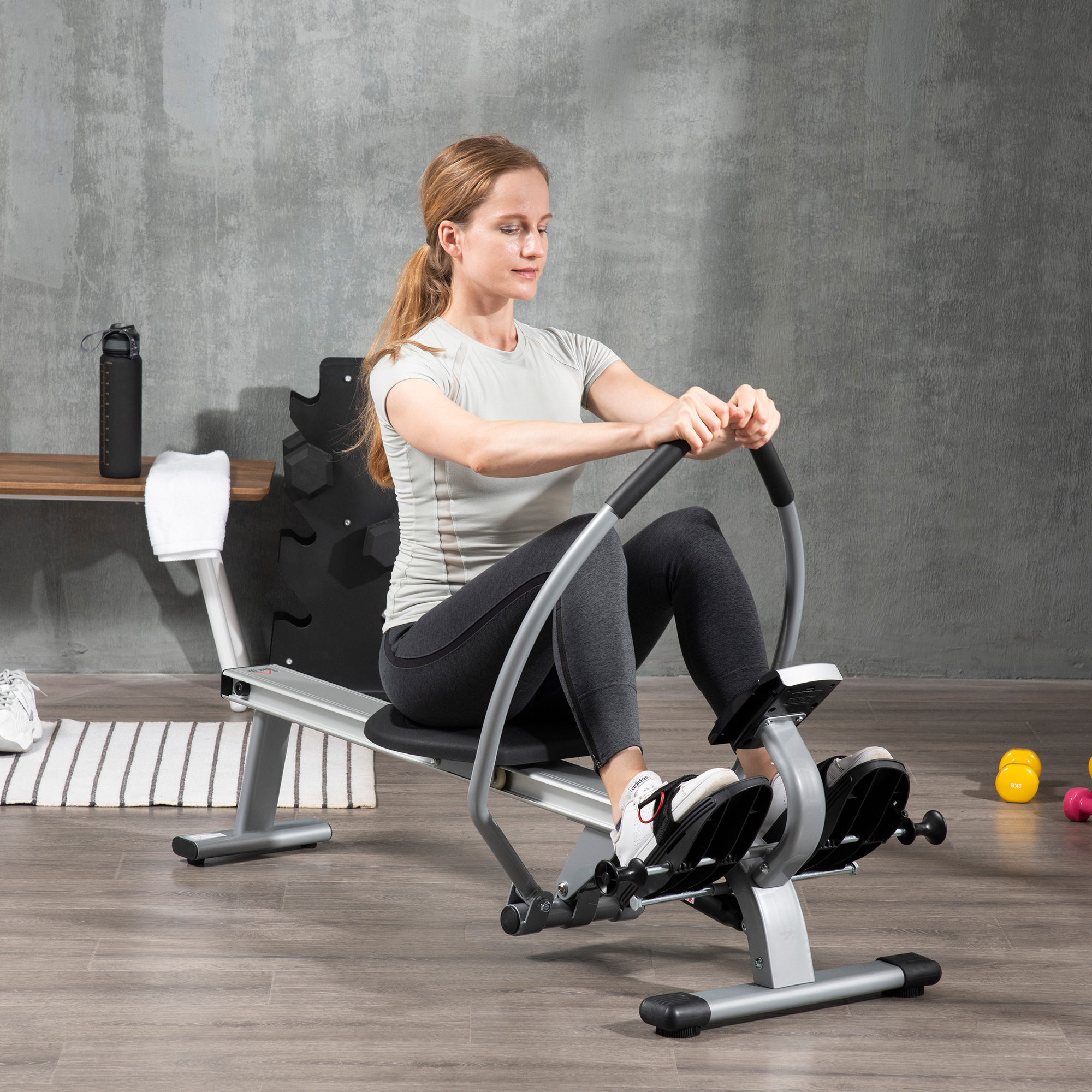 Donna che usa un vogatore in palestra. Altre attrezzature visibili. Muro grigio sullo sfondo.