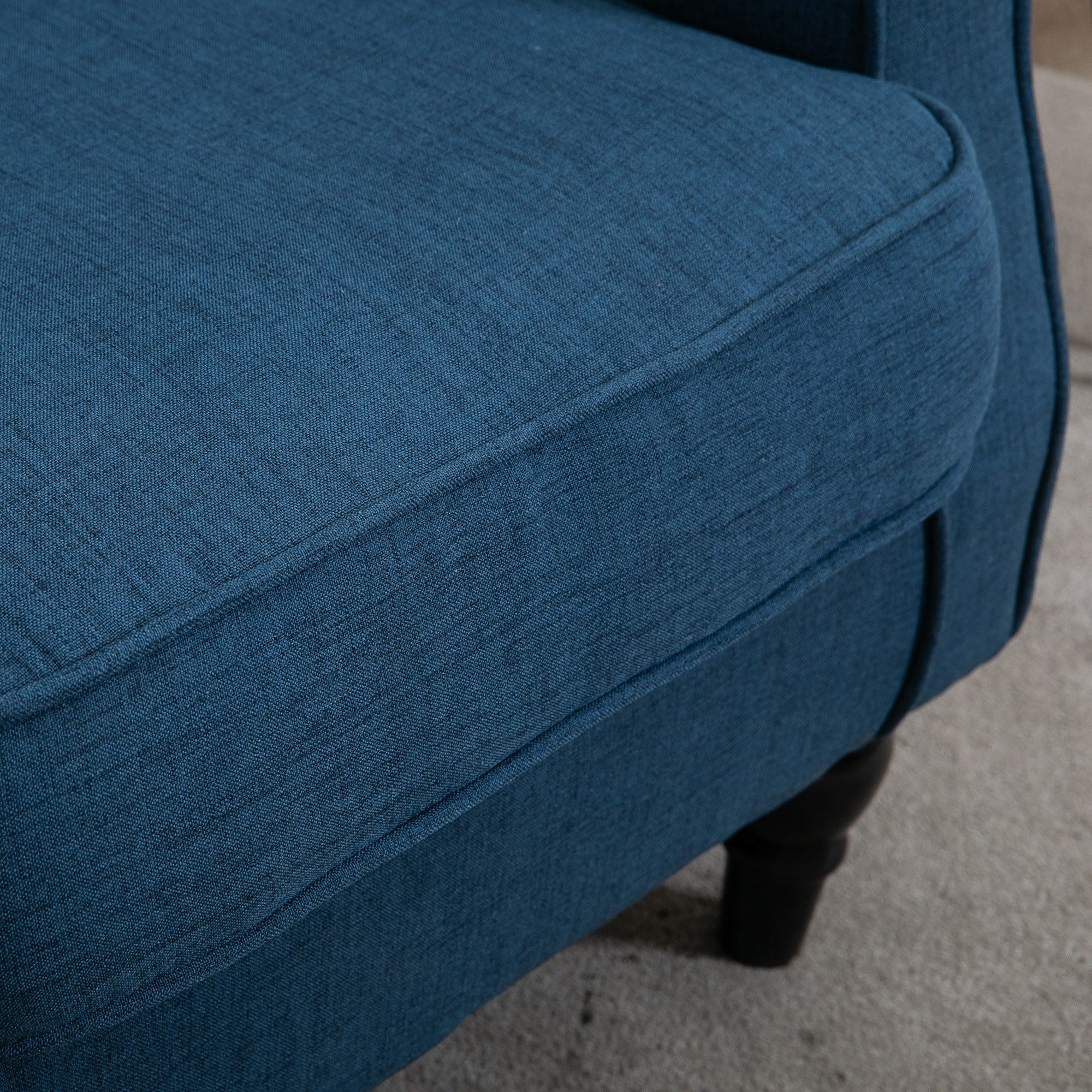 Primo piano di una poltrona in tessuto blu con gambe in legno scuro. Il tessuto è strutturato.