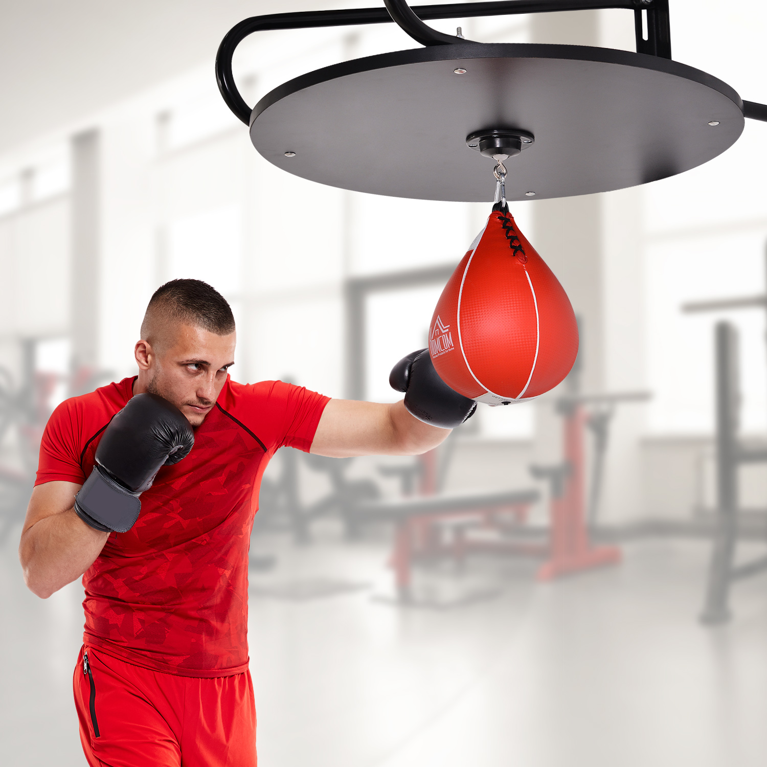 Uomo in maglietta rossa che boxa un sacco veloce rosso. Attrezzature da palestra sullo sfondo.