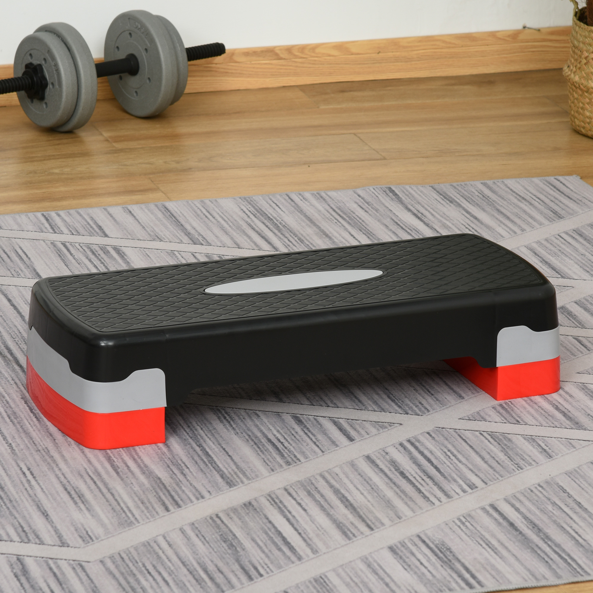 Piattaforma per step nera e rossa su un tappeto fantasia. Manubri visibili sullo sfondo.