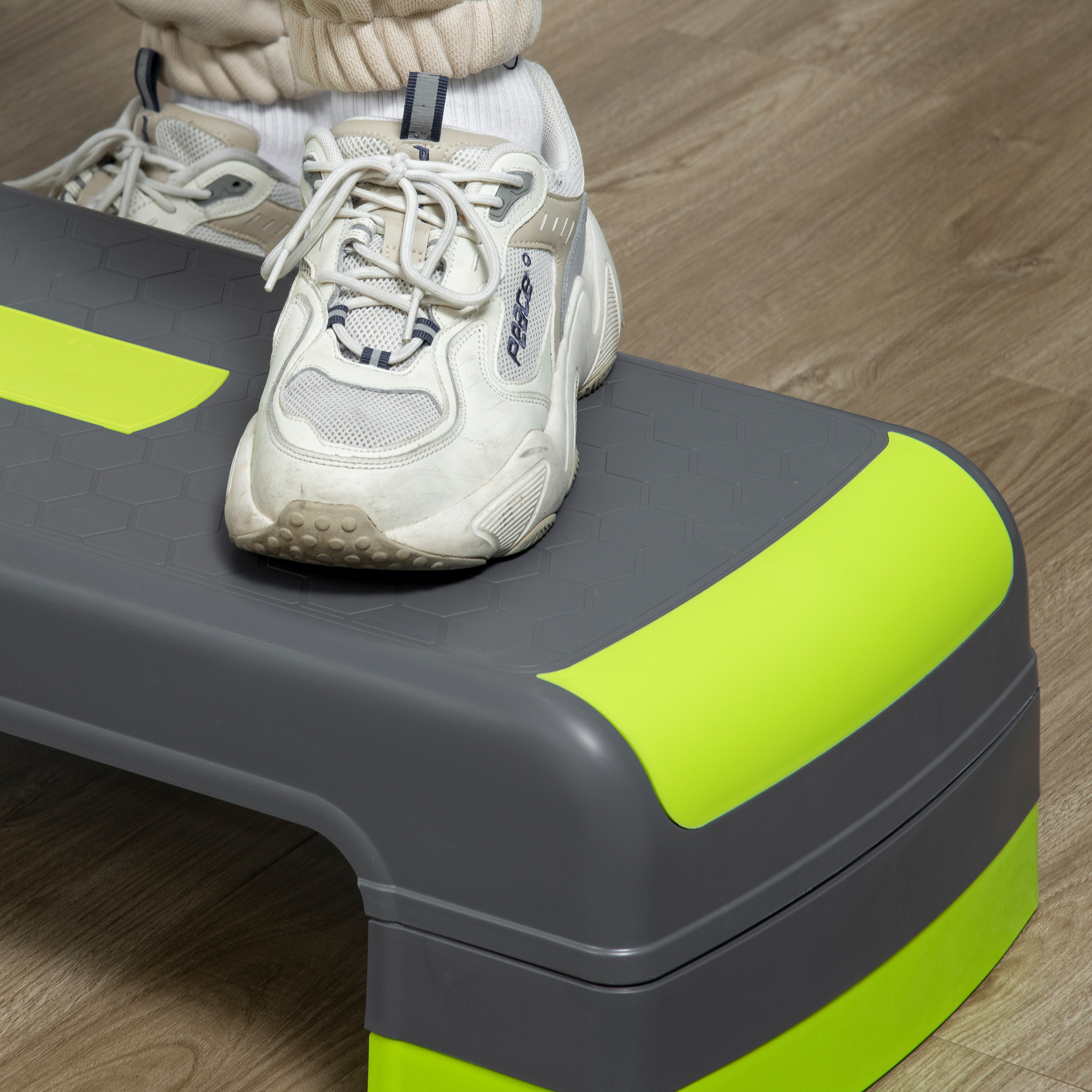 Persona con scarpe da ginnastica bianche su una piattaforma a gradini grigia e verde. Pavimento in legno sullo sfondo.