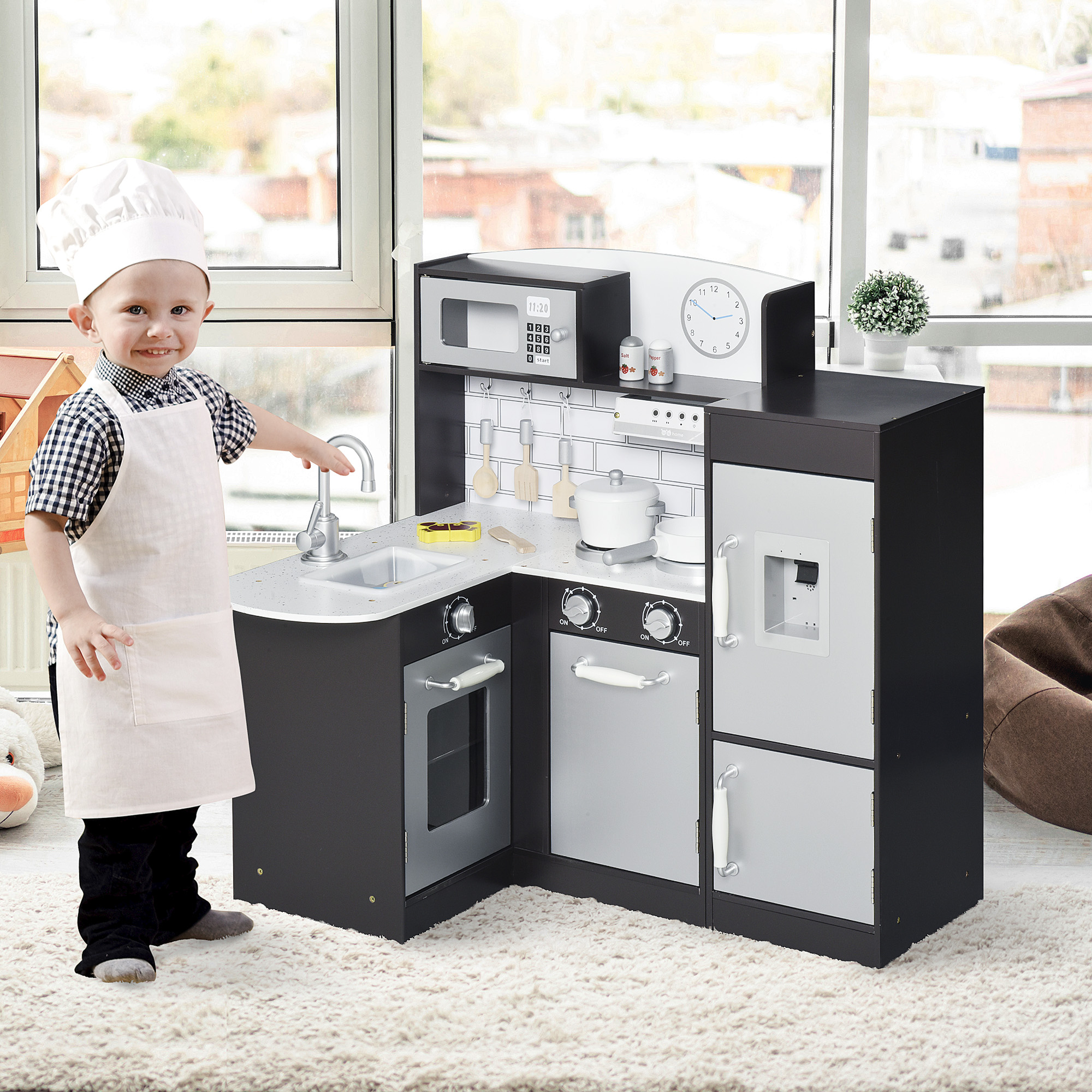 Ragazzino con cappello e grembiule da chef accanto a una cucina giocattolo. Sorridente.