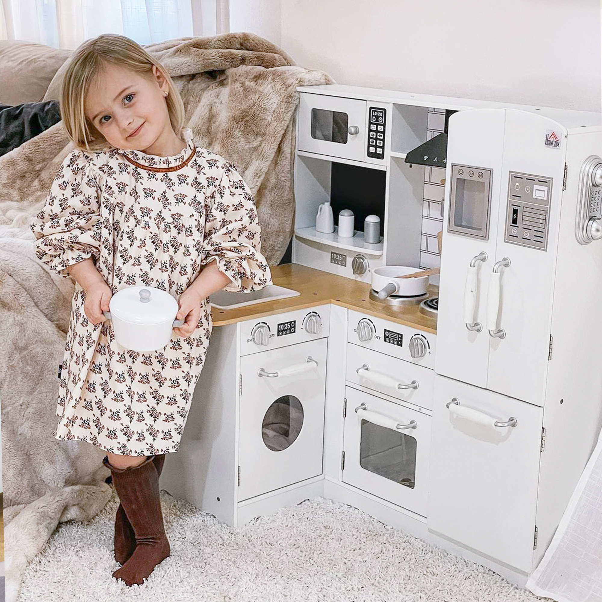 Una bambina posa accanto a una cucina giocattolo, tenendo una piccola pentola.