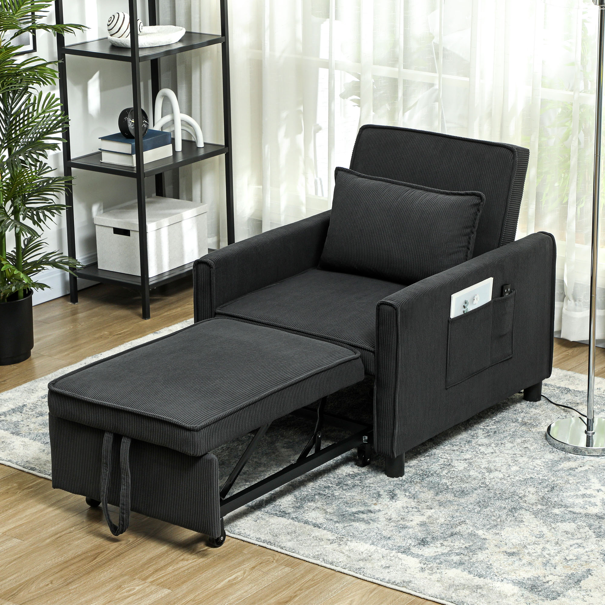 Poltrona convertibile grigio scuro con pouf, in una stanza con finestra e scaffali.
