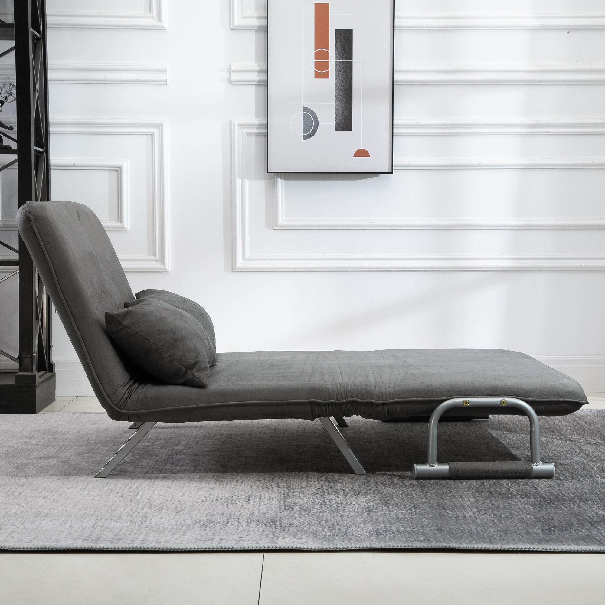 Divano grigio in stile futon con due cuscini contro un muro bianco con un'opera d'arte moderna.