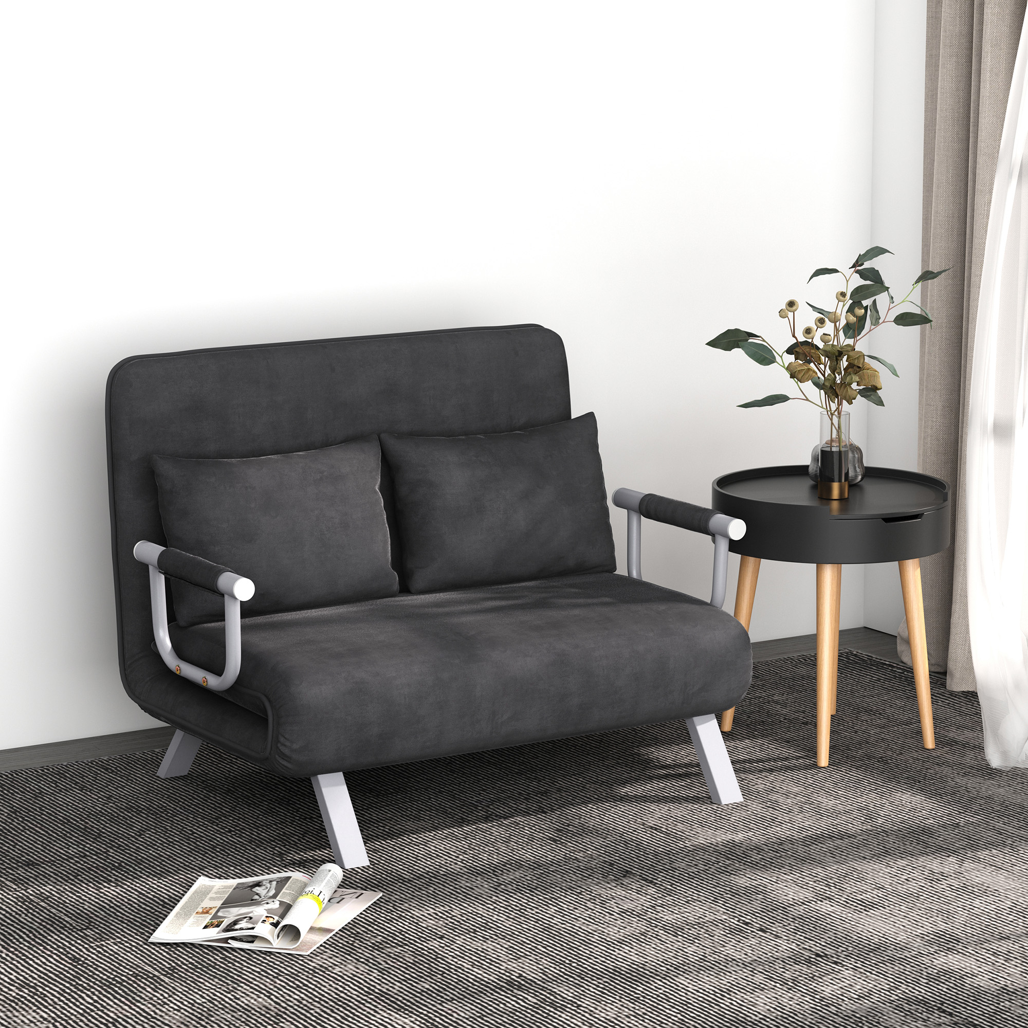 Sofá gris oscuro con dos almohadas, sobre una alfombra estampada. Una mesa pequeña con una planta al lado.