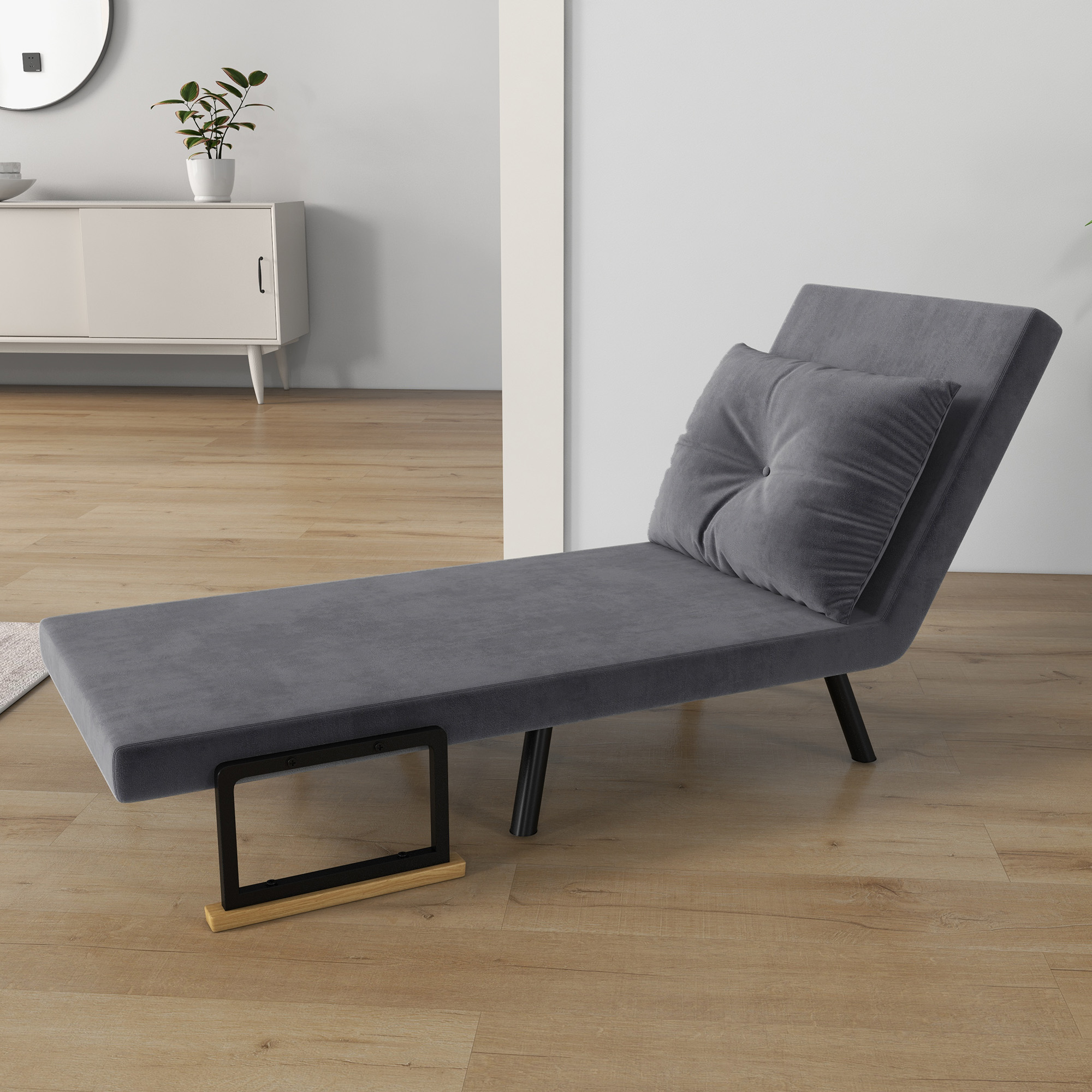 Una chaise longue grigia con un cuscino e un tablet su un supporto di legno. Un mobile bianco sullo sfondo.