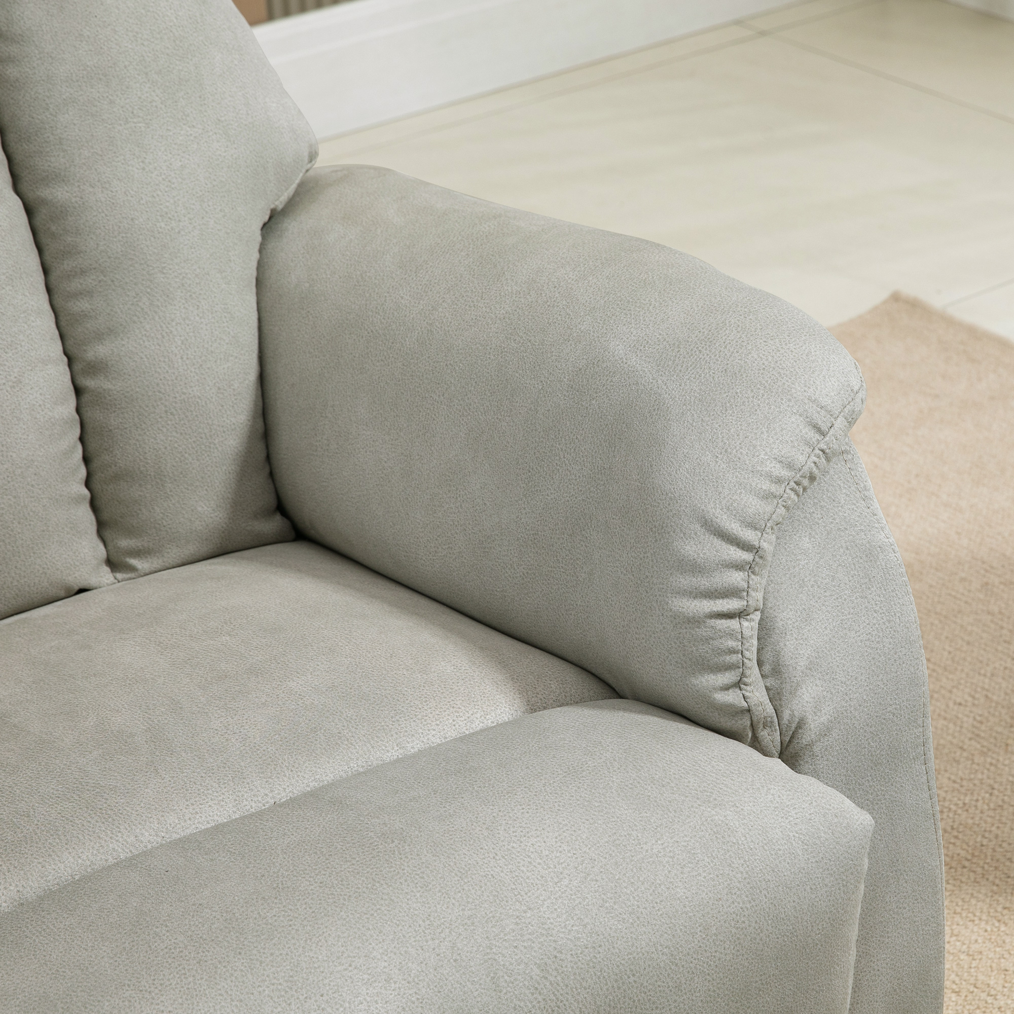 Primo piano del bracciolo grigio di una poltrona reclinabile. Tappeto beige sullo sfondo, parete bianca.